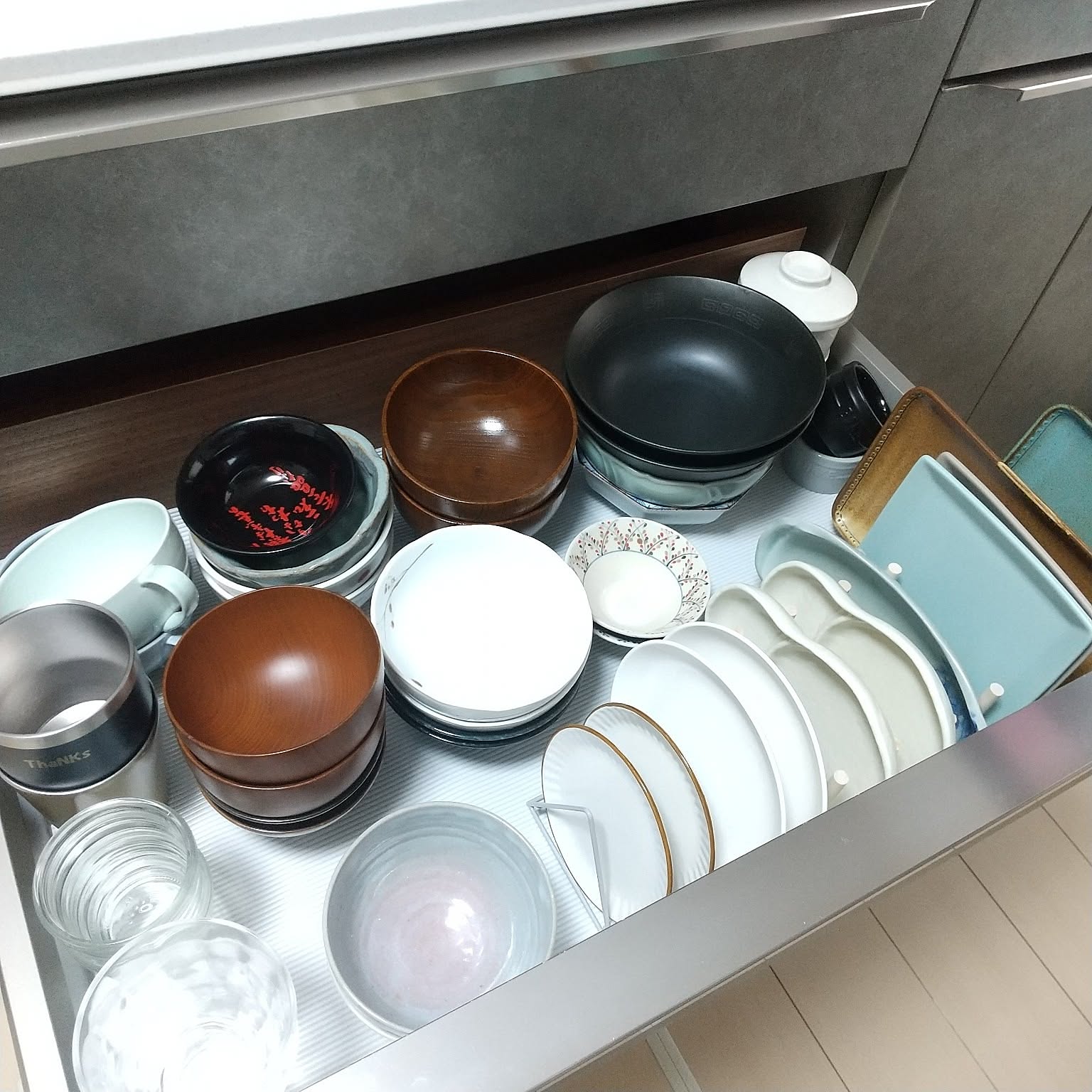 Kitchen drawer with stacked small plates, bowls, cups, and utensils.