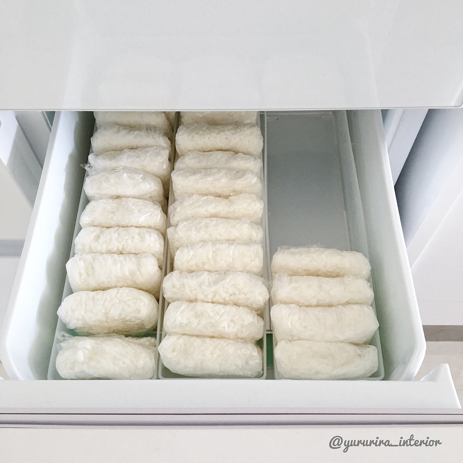 A freezer drawer neatly lined with individually wrapped rice portions in a compact Japanese kitchen.