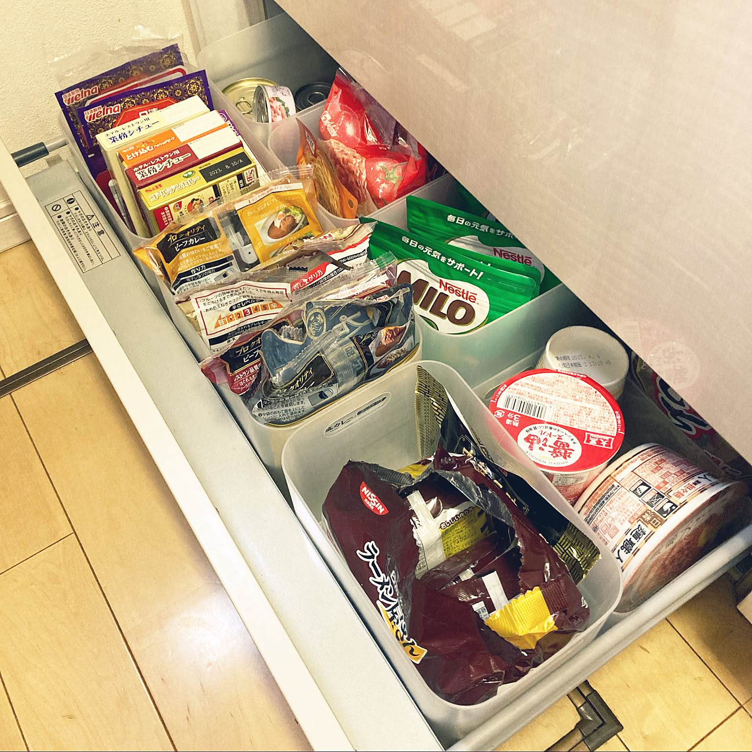 A pantry drawer with retort packs, cup noodles, cans, packets, and snacks sorted into shallow bins.
