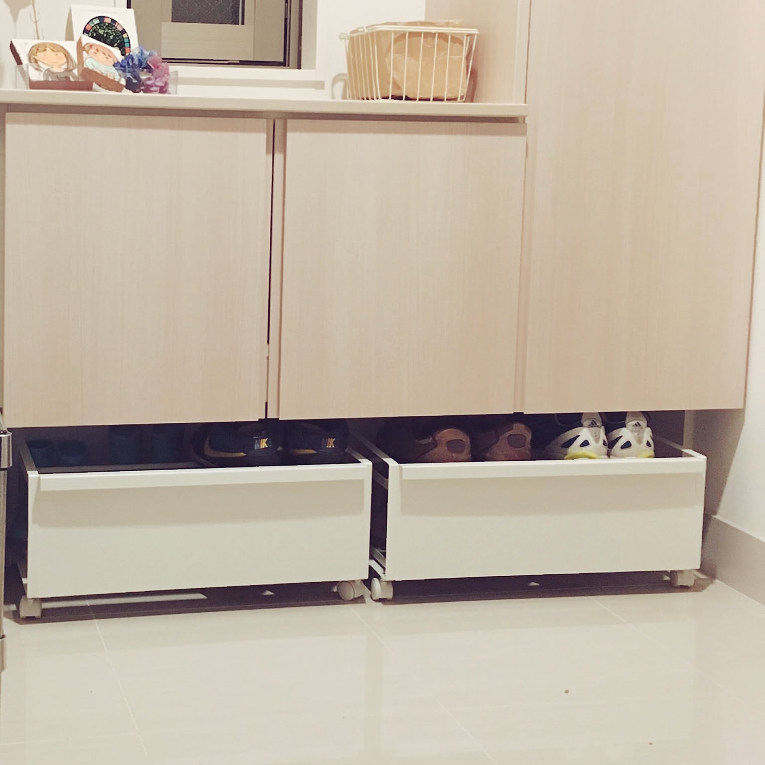 Two white rolling shoe wagons stored under a shoe cabinet in a narrow entryway.