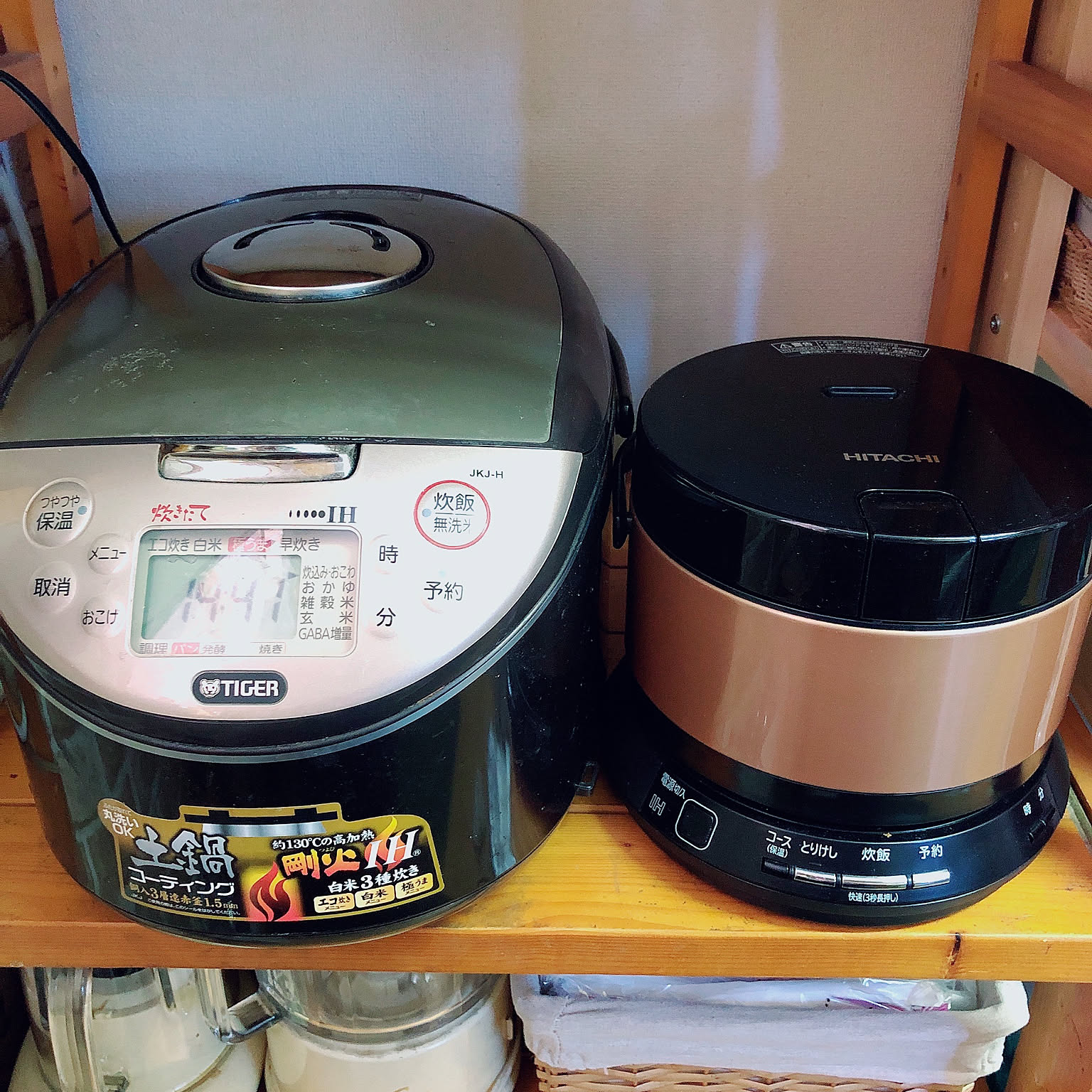 A compact Hitachi 2-go rice cooker placed beside a larger Tiger rice cooker on a shelf.
