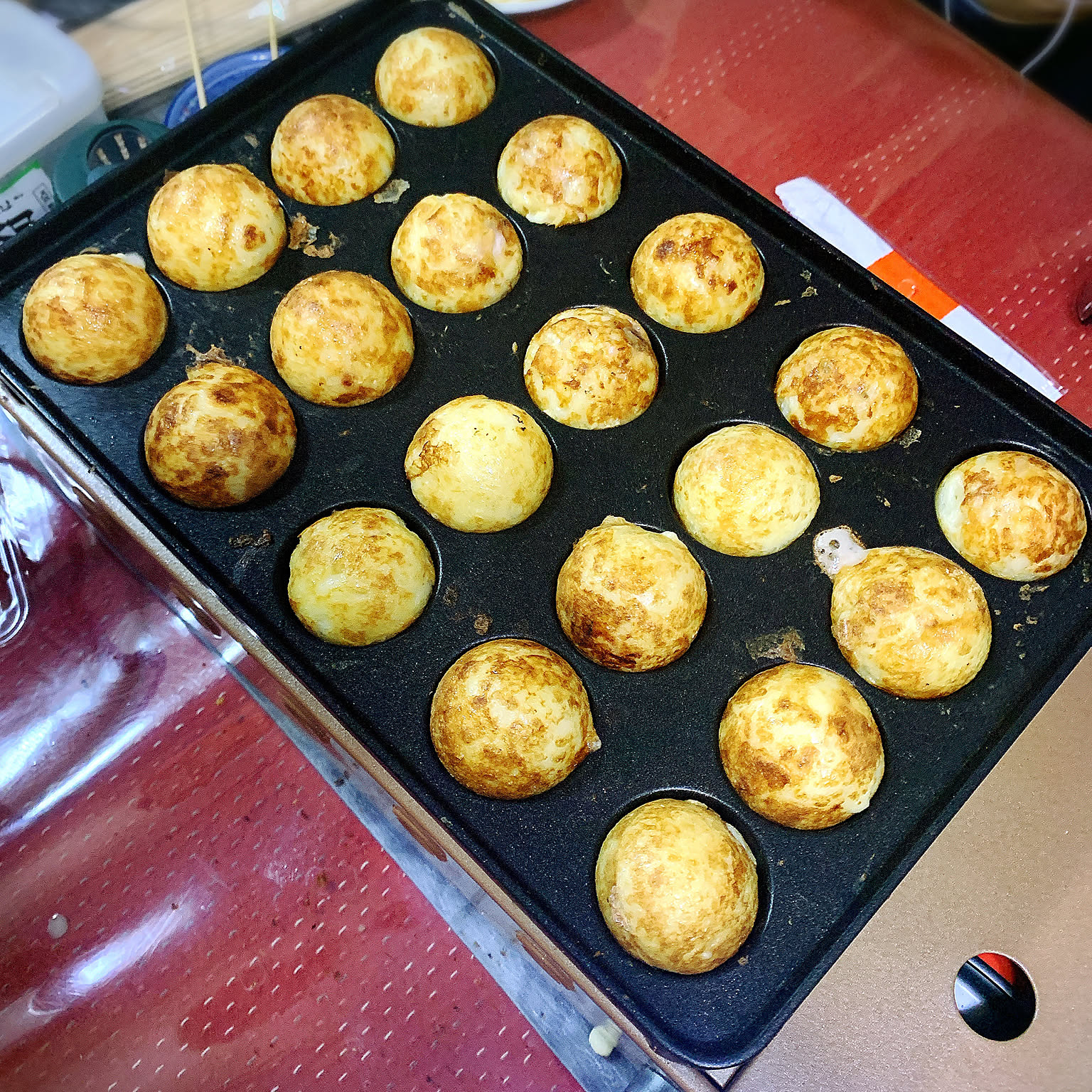 Golden takoyaki cooking in the round wells of an Iwatani takoyaki plate.