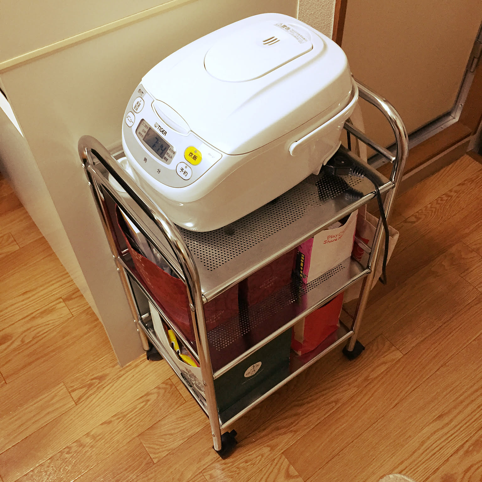 A white compact rice cooker placed on a narrow rolling kitchen cart.