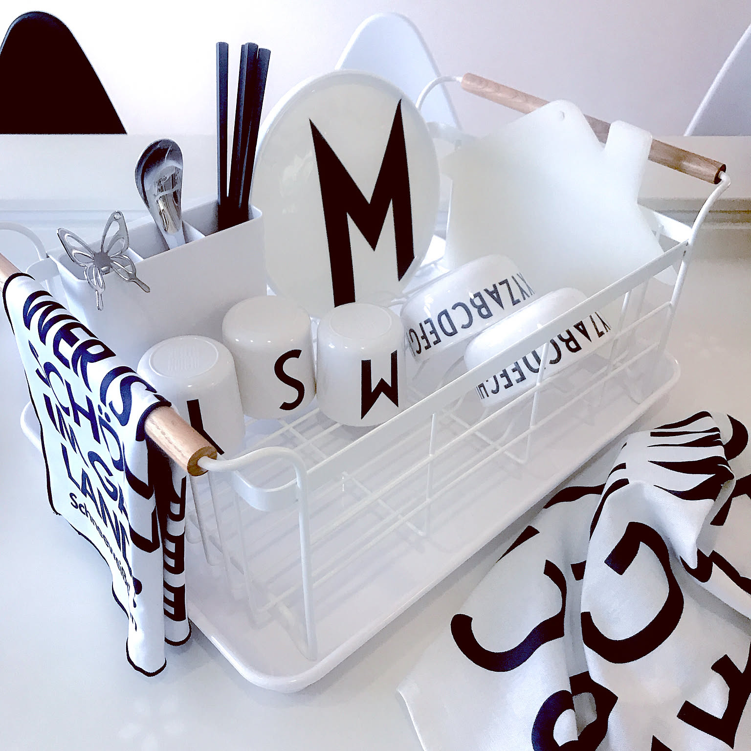 A white Tosca dish rack with wood handles holding plates, cups, and utensils.