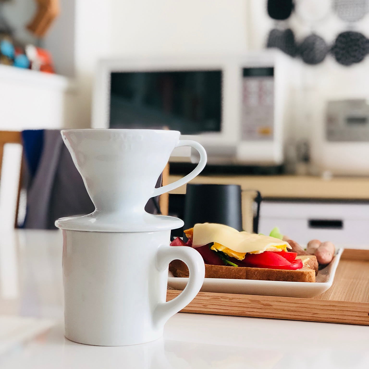 A white HARIO V60 ceramic dripper on a mug beside a breakfast tray.