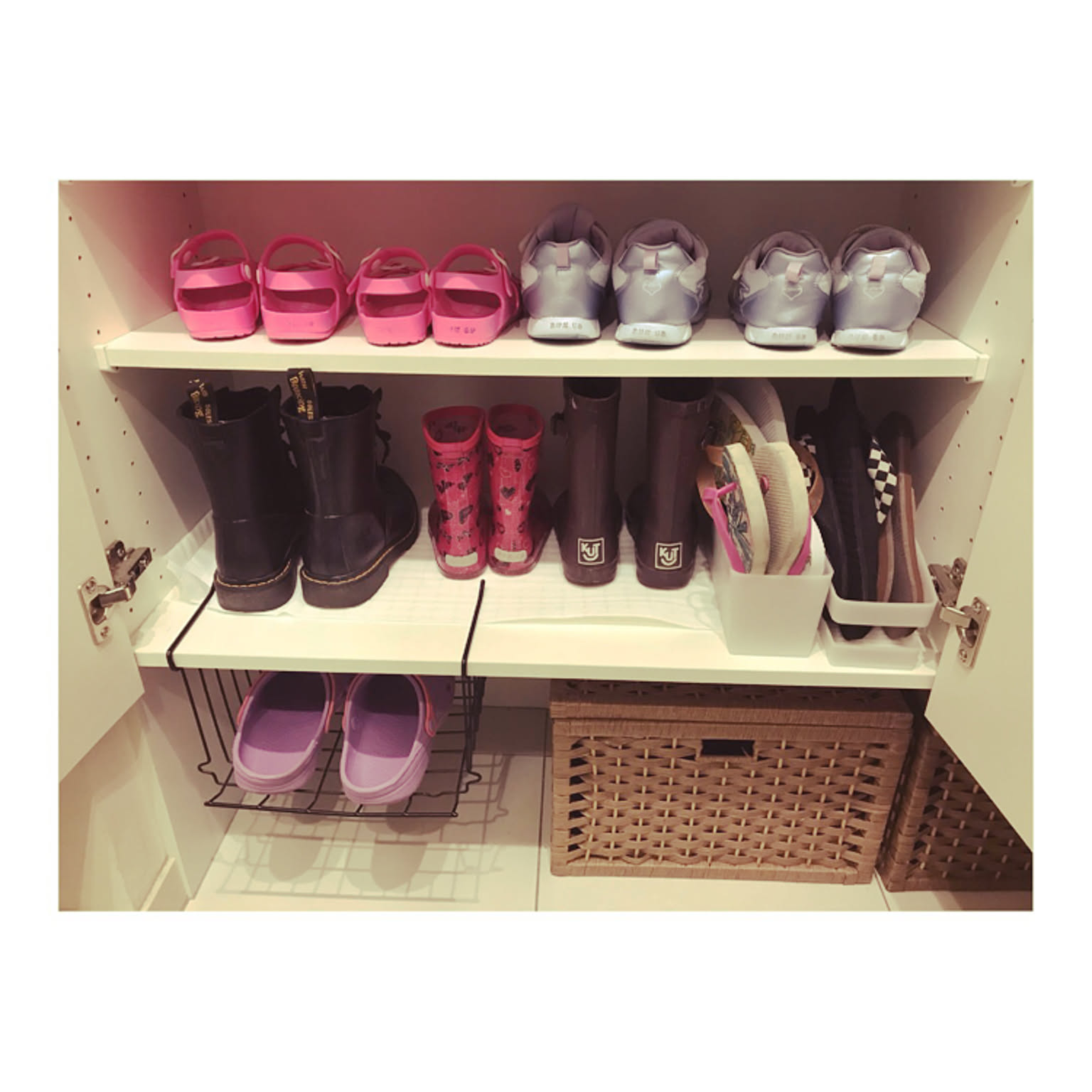 Kids' shoes, rain boots, sandals, and baskets arranged inside a low shoe cabinet.