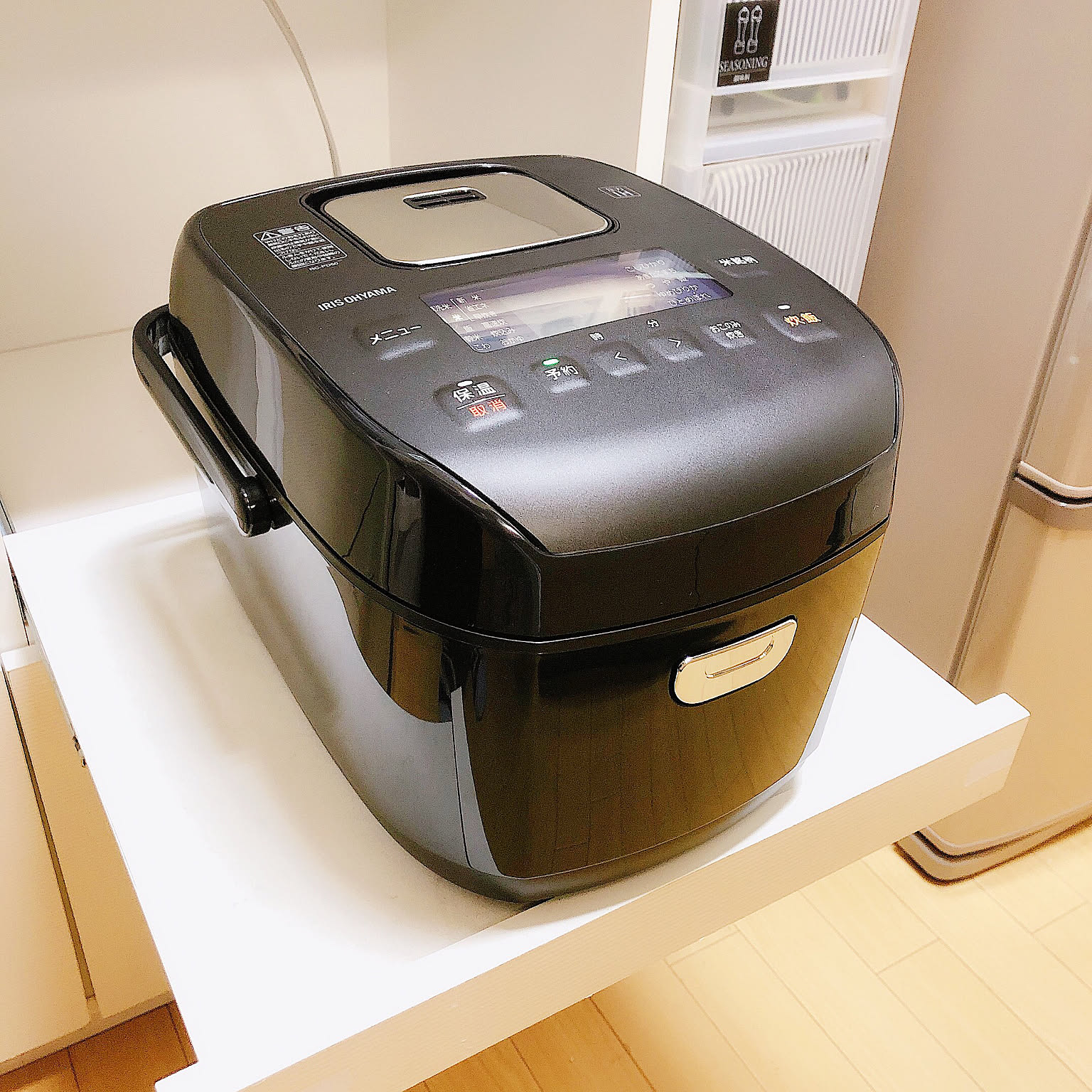 A black 5.5-cup rice cooker shown clearly on a small white shelf.