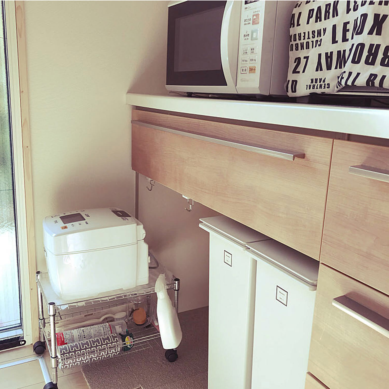 A white 5.5-cup rice cooker parked on a slim rolling cart under a kitchen counter.