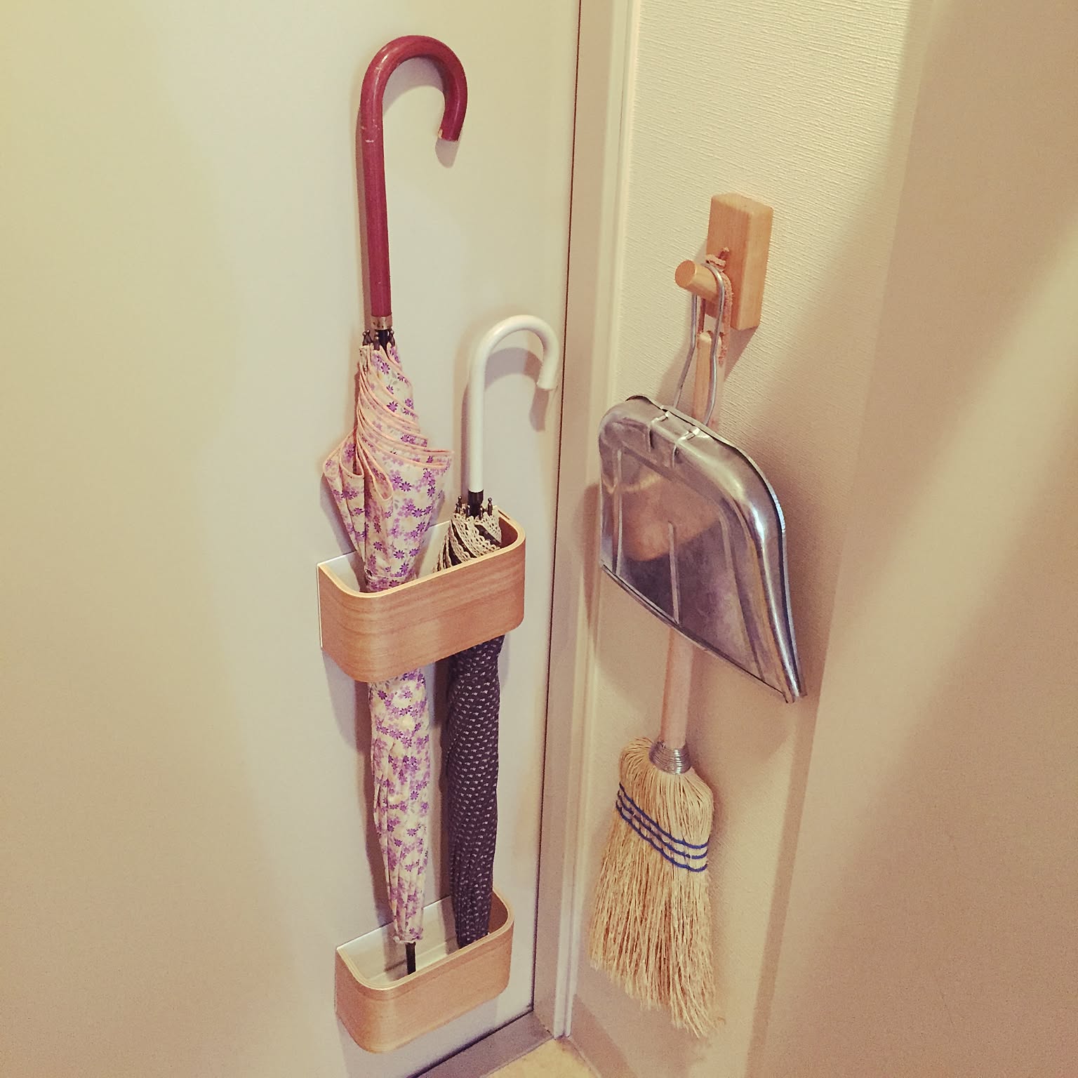 A narrow entryway wall using a slim umbrella holder and hanging broom and dustpan.