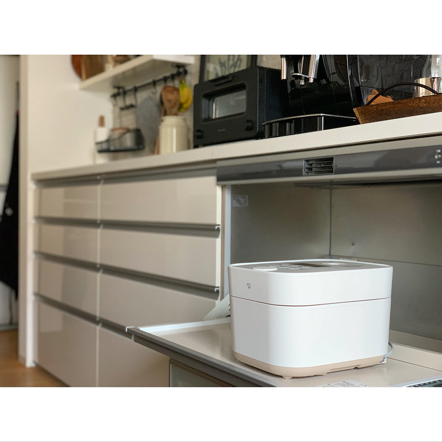 A white square Zojirushi STAN rice cooker on a pulled-out shelf, with a toaster and coffee maker on the counter behind
