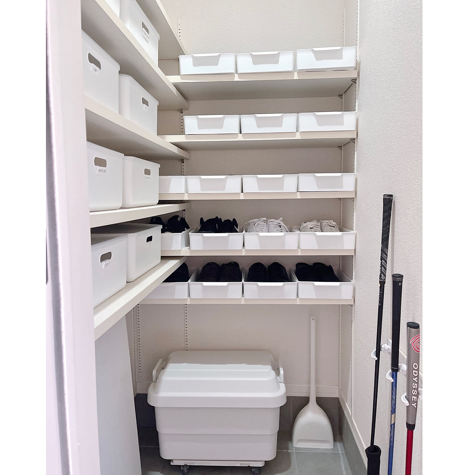 A white shoe closet with labeled bins, shoe trays, and cleaning tools kept in a clear vertical layout.