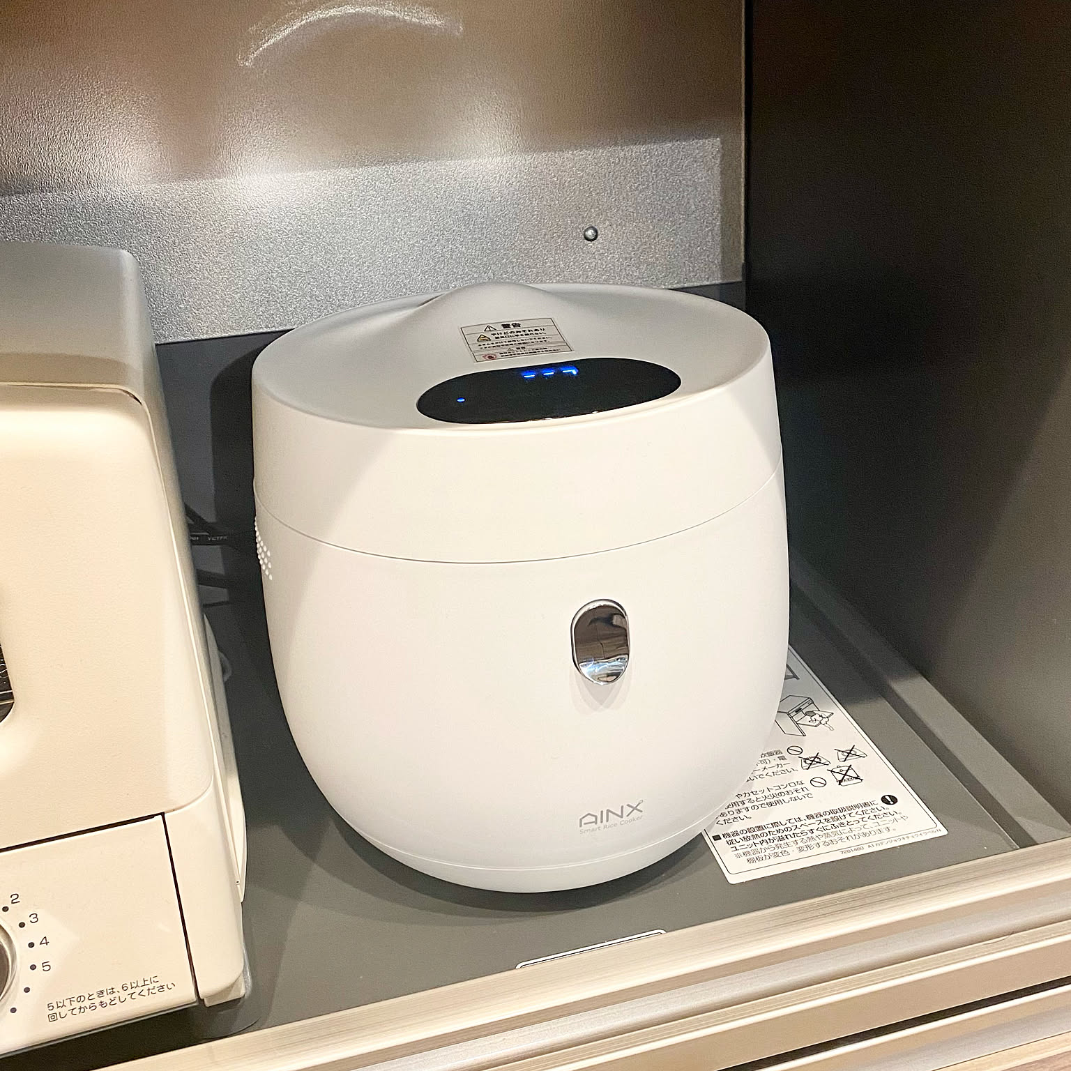 A compact white rice cooker with a touch panel and brown rice mode in a Japanese kitchen.