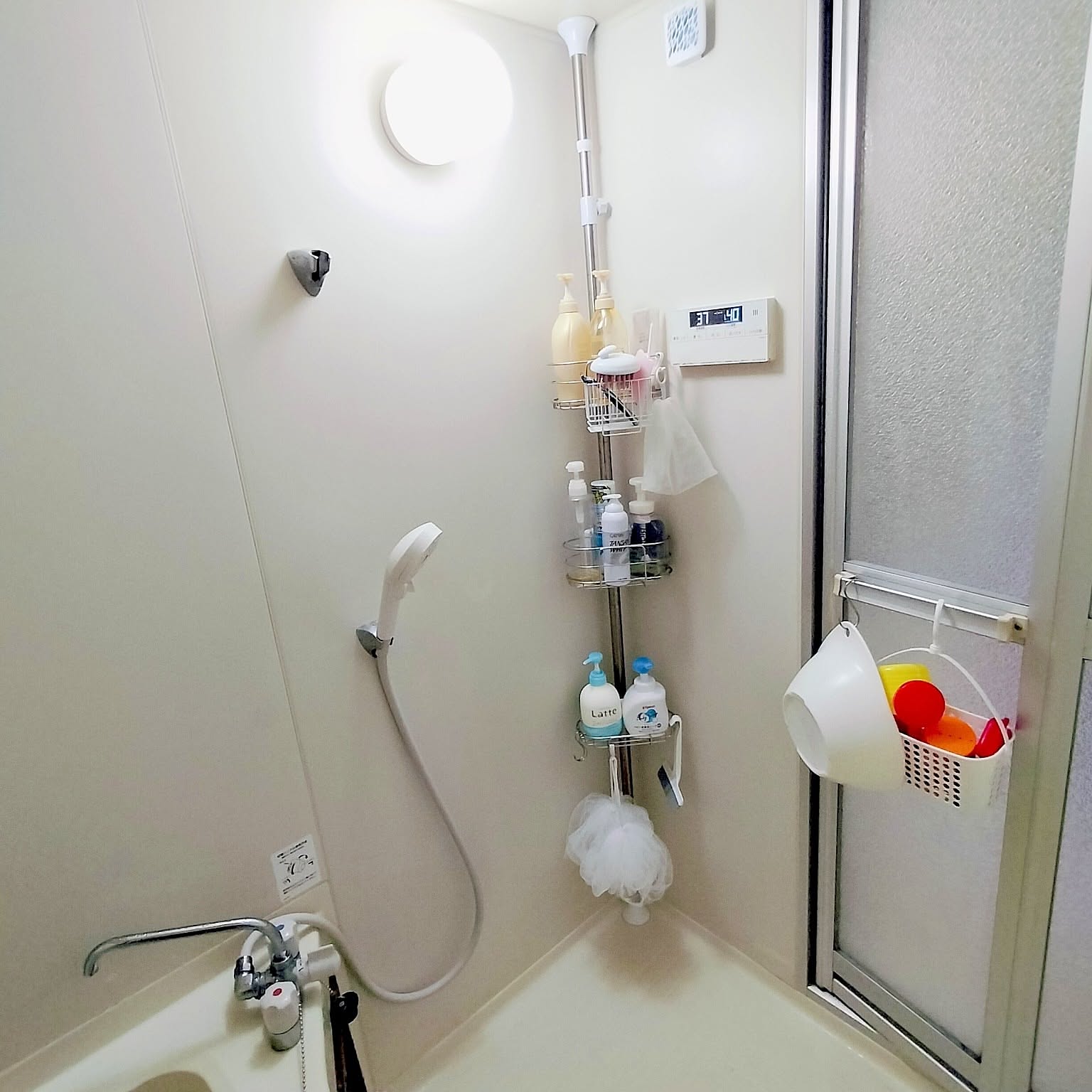 A very small Japanese unit bathroom using a vertical tension pole with wire baskets for toiletries.