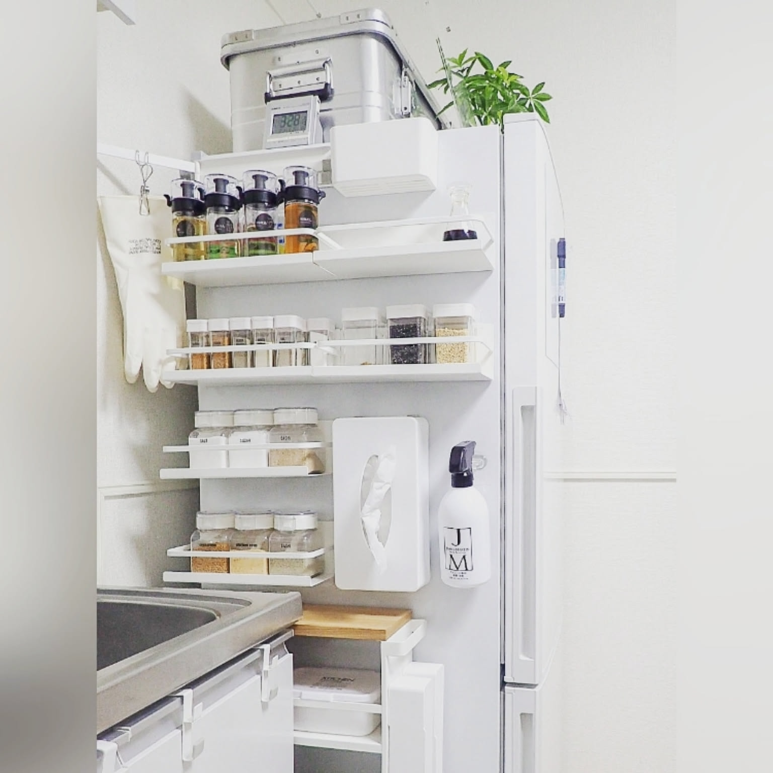 The side of a refrigerator in a Japanese kitchen holding tiered magnetic racks filled with spices, a magnetic tissue case, and cleaning gloves
