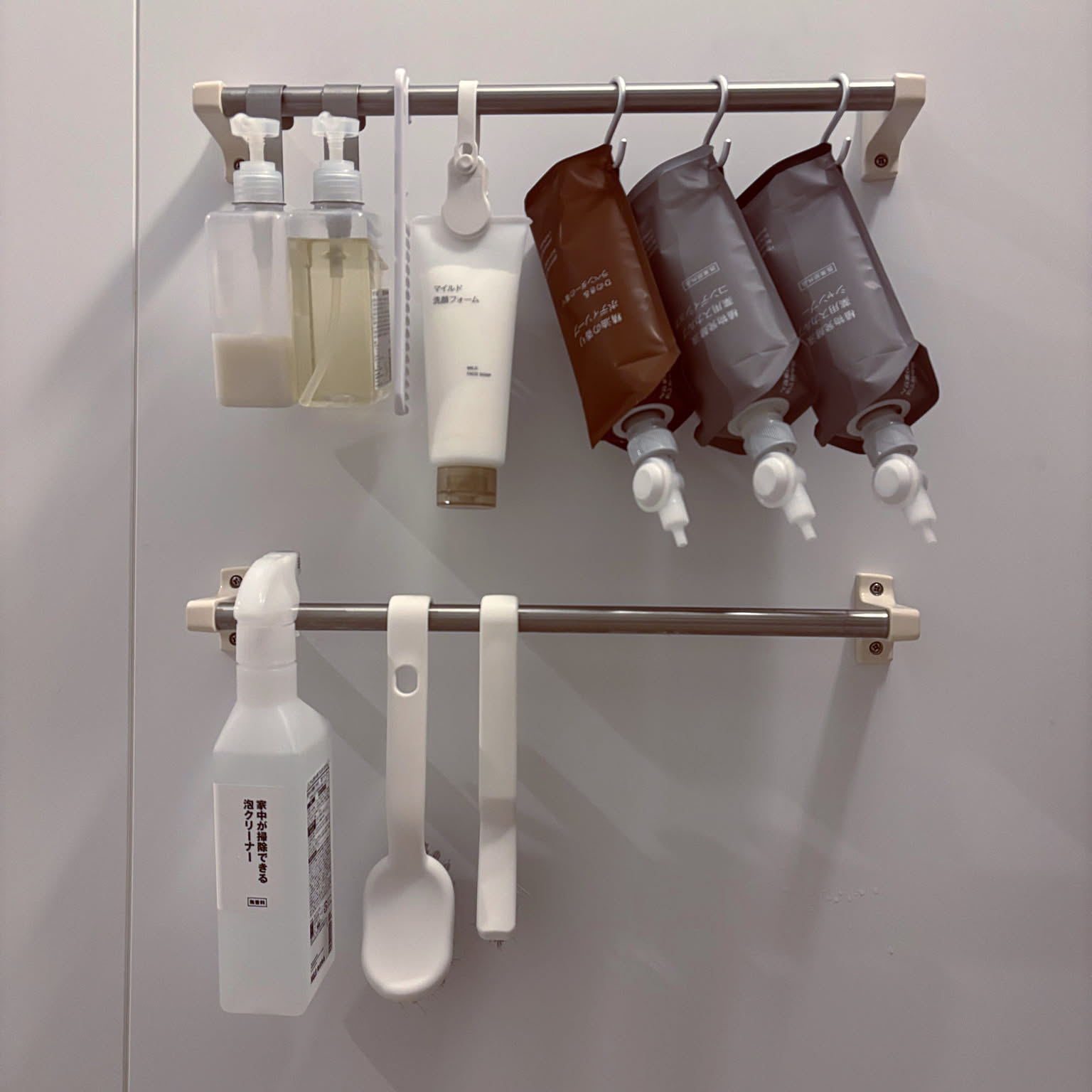 Shampoo refill pouches, soap dispensers, and cleaning tools hanging from two bathroom rails.