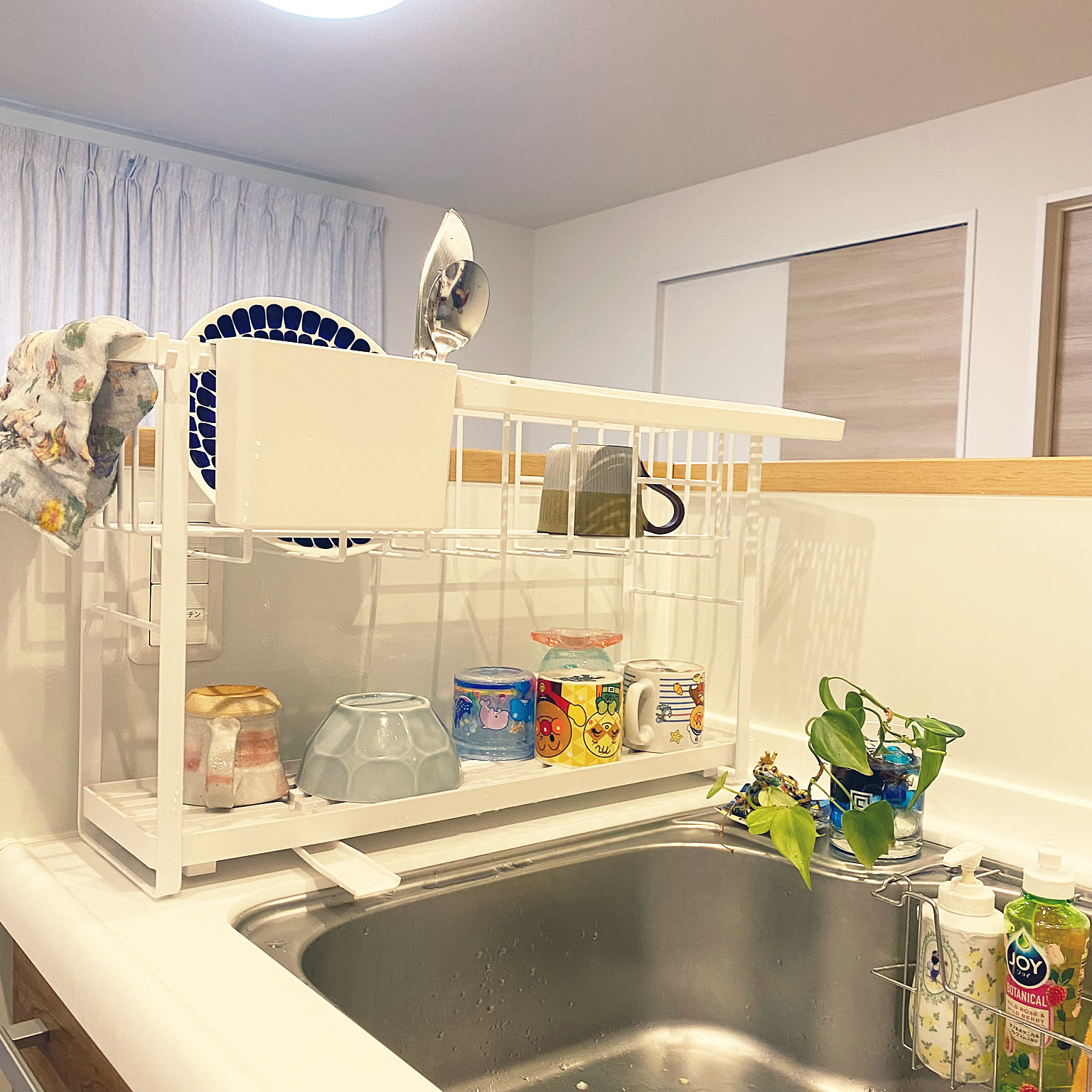 A two-tier white Yamazaki Tower dish rack using vertical space beside a small sink.