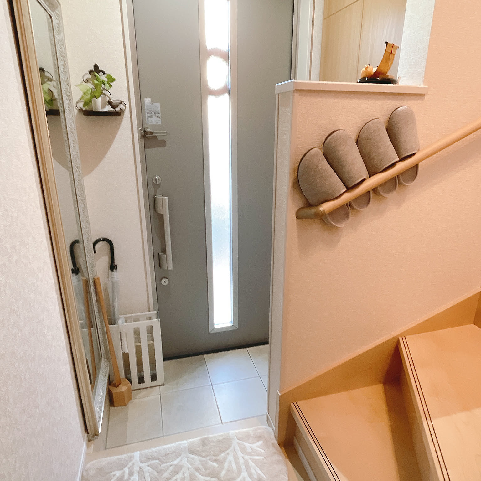 A bright narrow Japanese entryway with slippers stored on a wall rail and umbrellas contained beside the door.