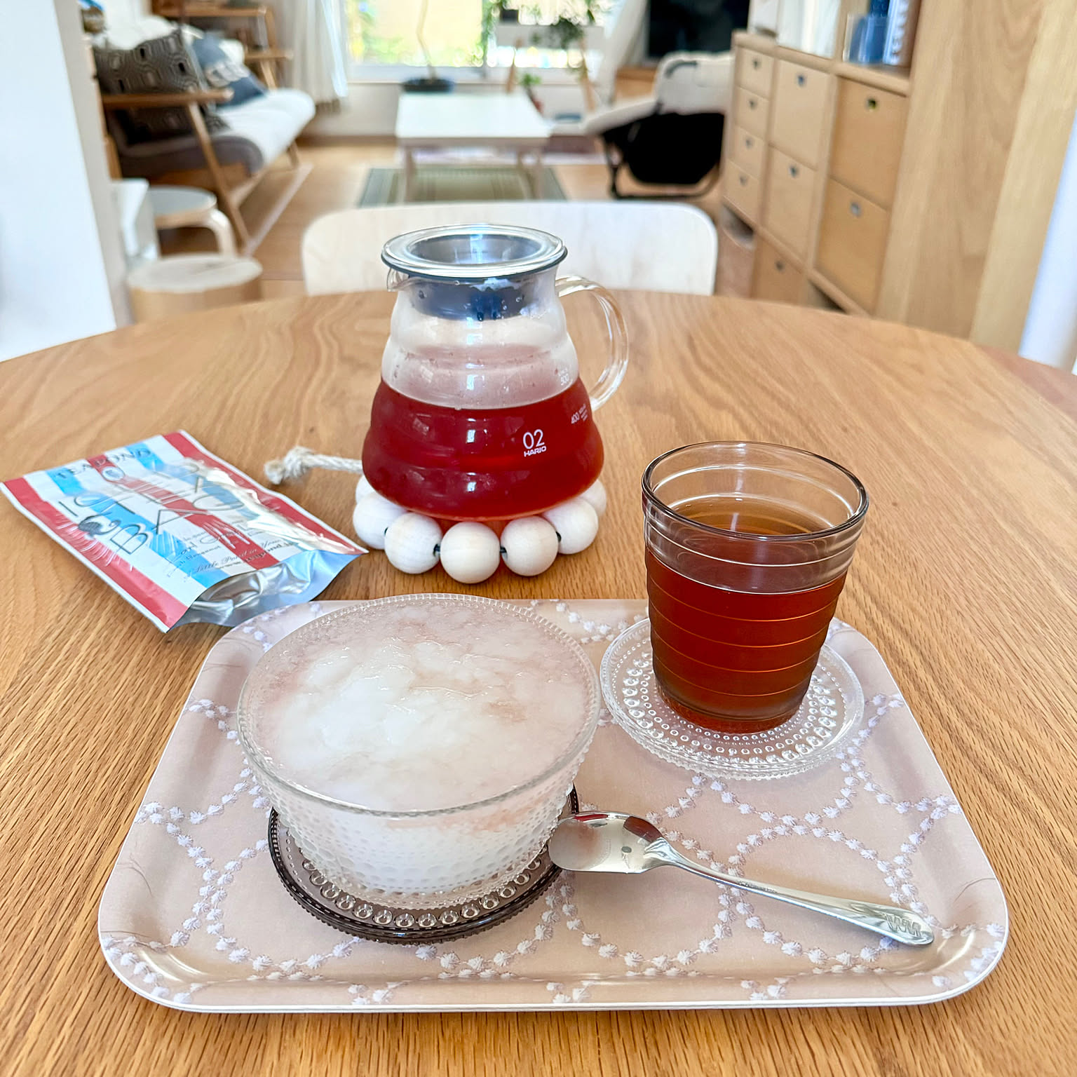 A HARIO V60 glass server holding tea on a wooden table in a bright dining room.