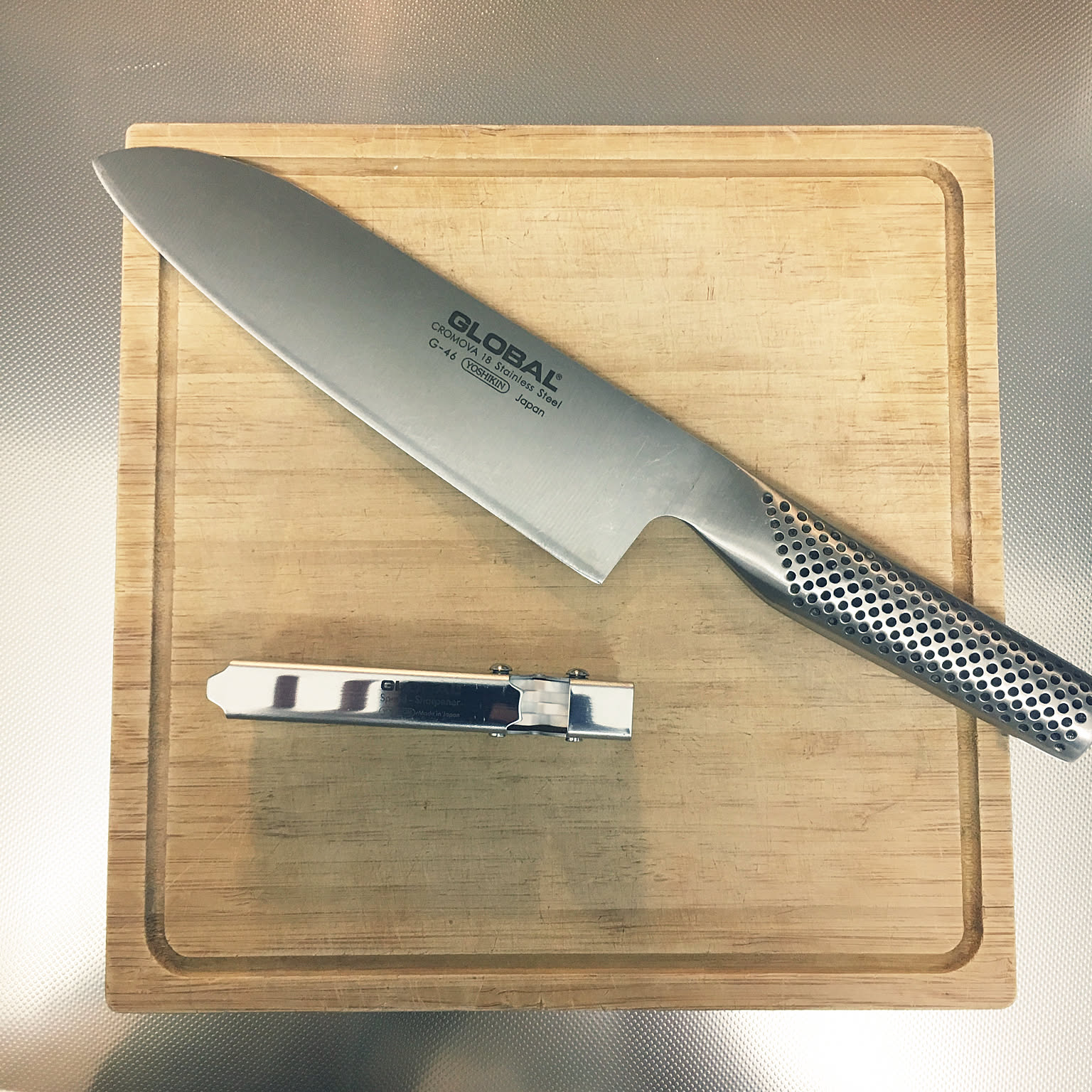 Global Japanese knife and small pull-through sharpener on a cutting board.