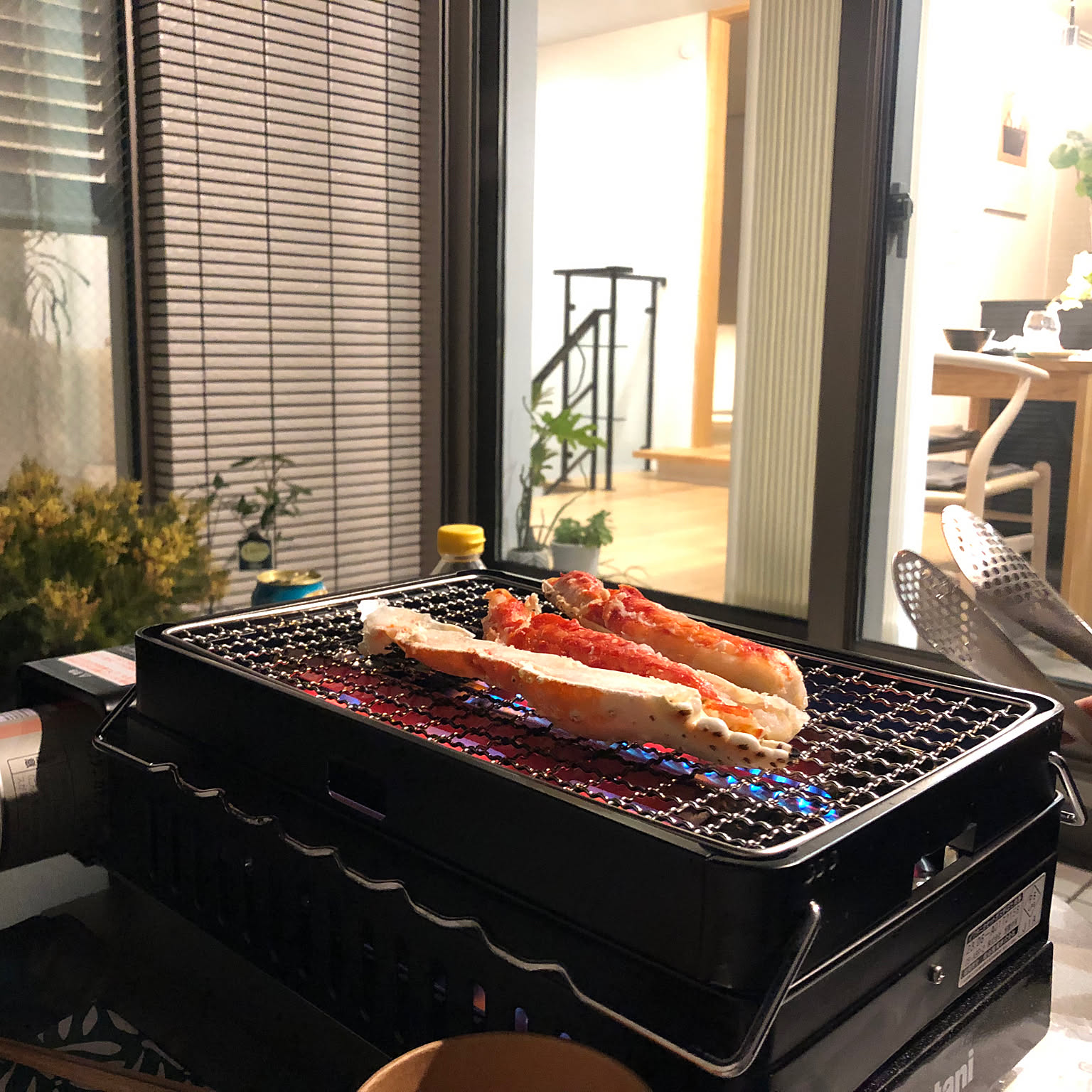 An Iwatani Aburiya II robata grill cooking crab legs on a balcony table.