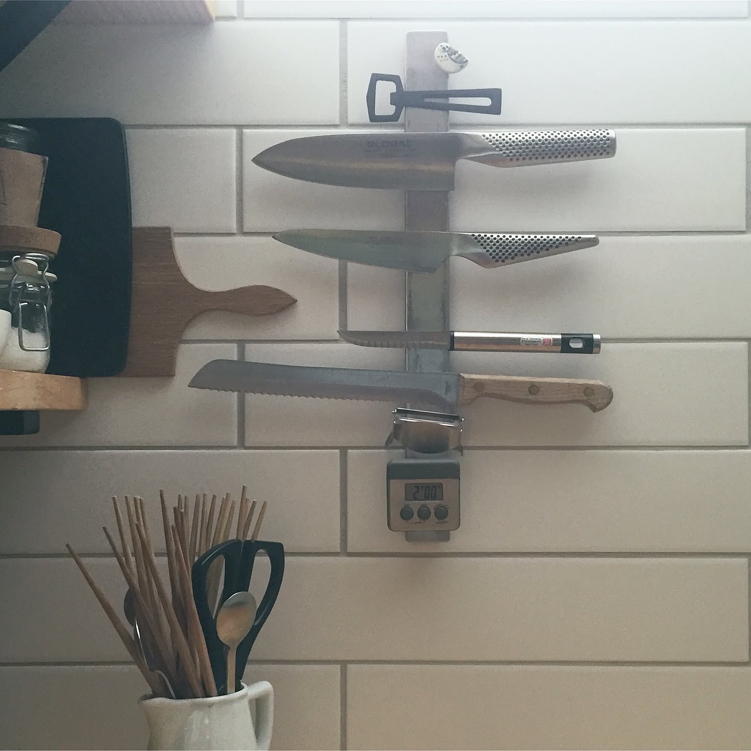 Japanese kitchen knives stored on a magnetic wall rack in a tiled kitchen.