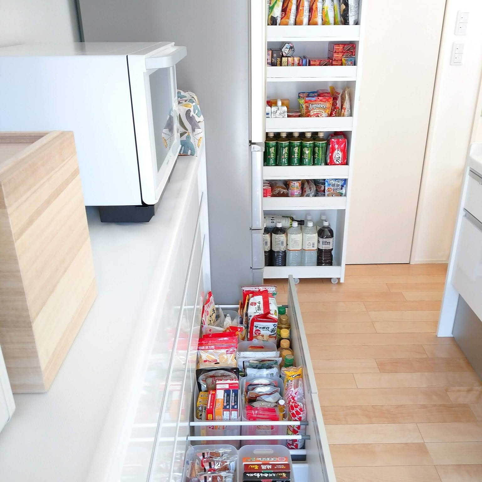 A small kitchen using a slim rolling cart beside the refrigerator and a drawer to store pantry food and bottled drinks.