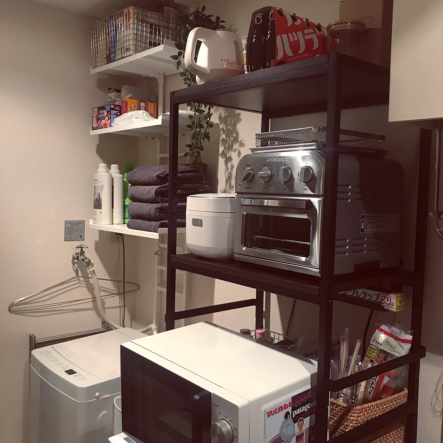 A compact white rice cooker stored on a black appliance rack beside a toaster oven and microwave.