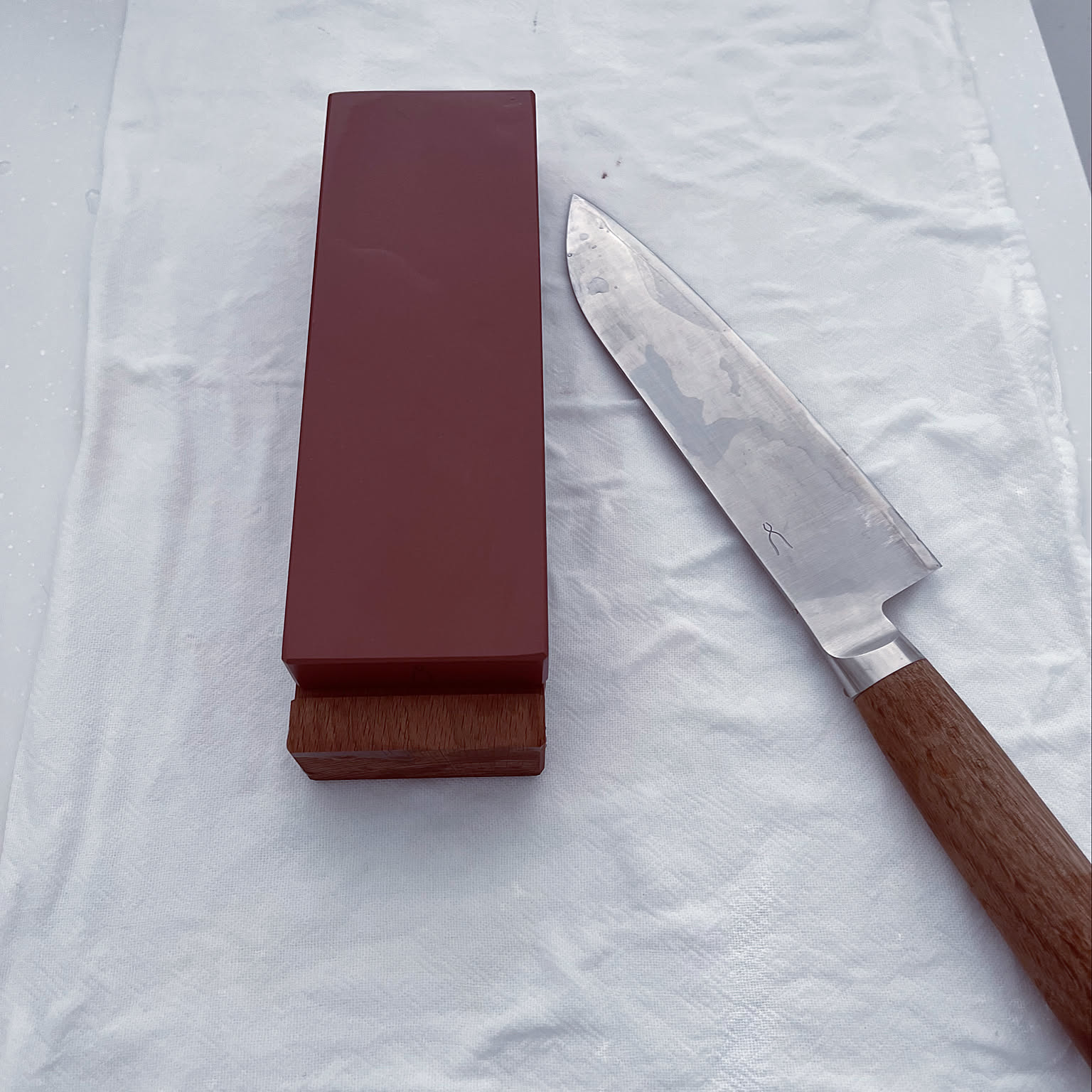 Japanese kitchen knife and whetstone arranged on a white towel.