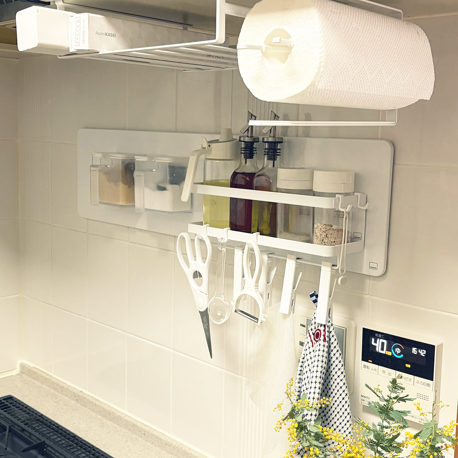 A white Yamazaki Tower magnetic panel system holding spices, paper towels, scissors, hooks, and small kitchen tools above a counter.