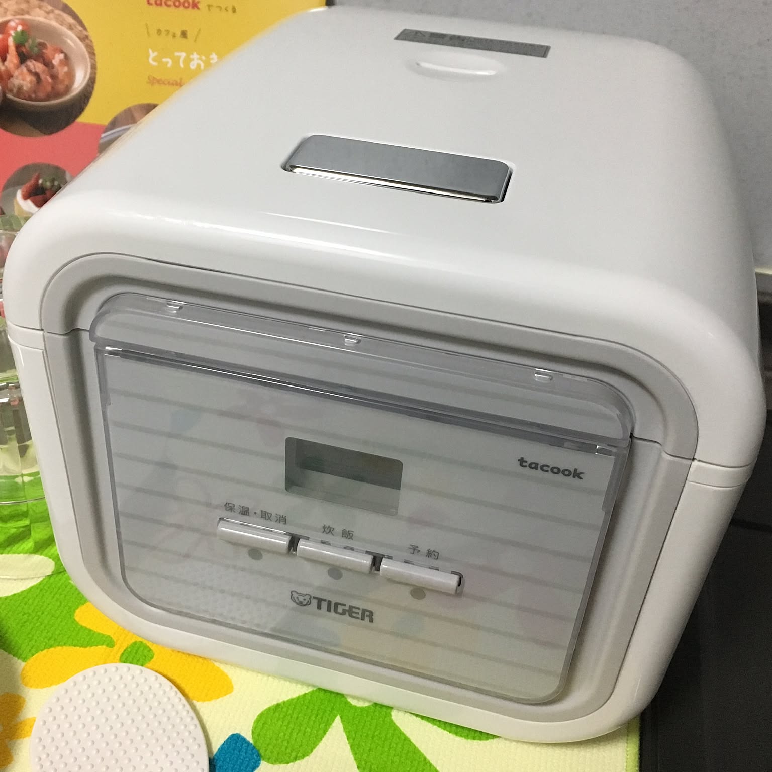 A compact white Tiger tacook rice cooker shown close-up beside its cooking plate.