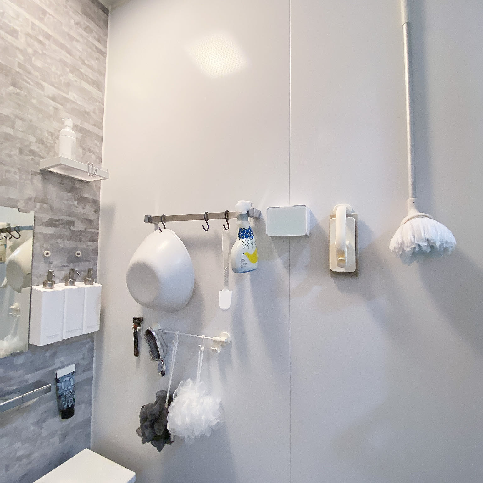 A bathroom wall with the basin, brushes, squeegee, slippers, and bath puffs stored in separate hanging positions.