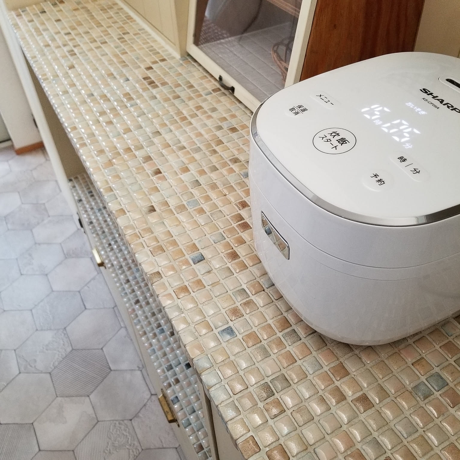 A white rice cooker placed in a cozy kitchen with everyday cooking tools nearby.