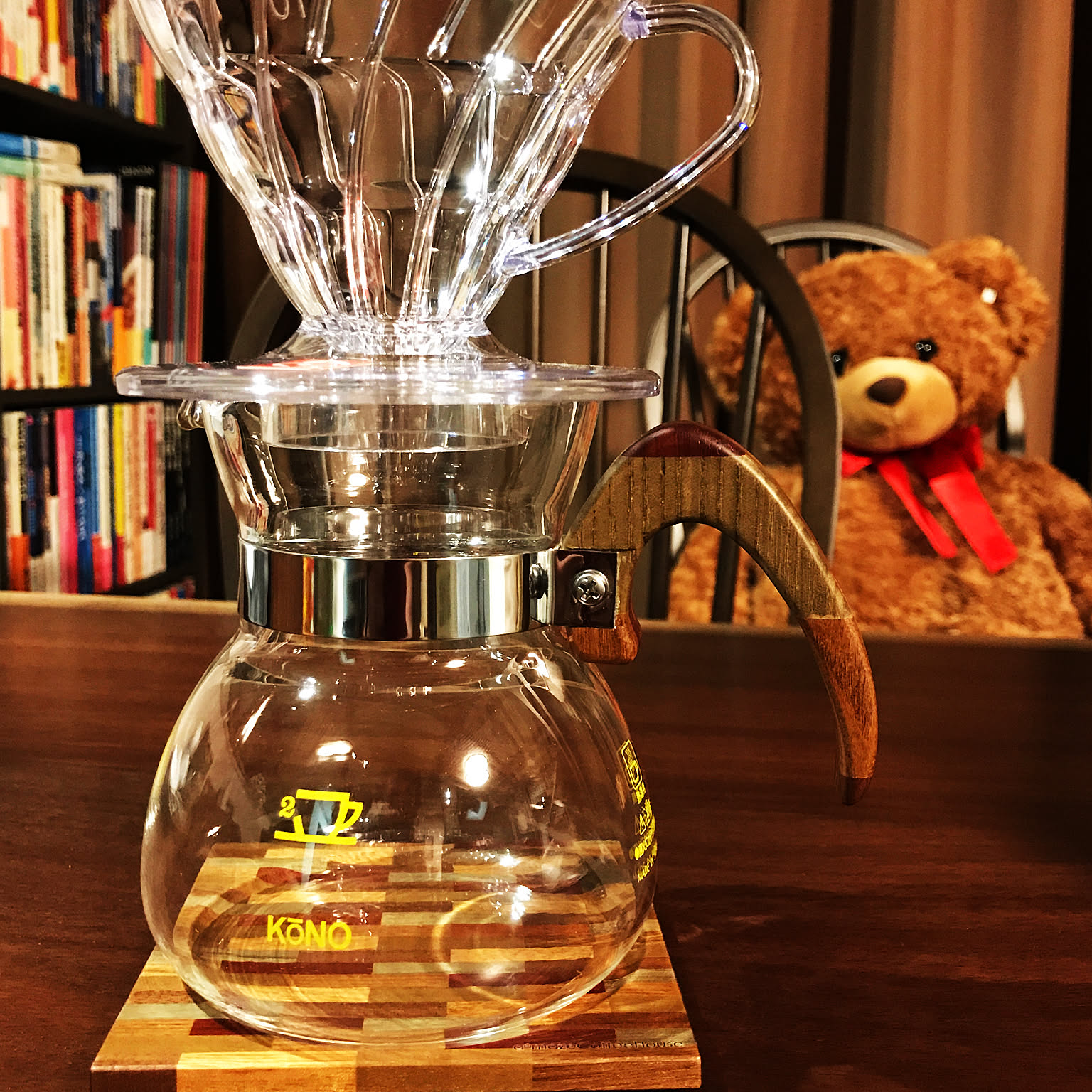 A clear V60-style dripper on a glass server in a warm home coffee setup.