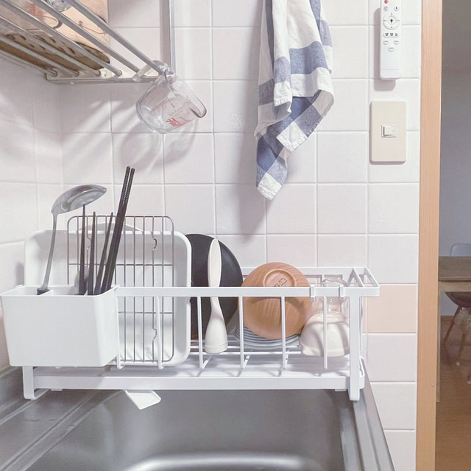 A slim white Yamazaki dish rack holding plates and glasses beside a compact kitchen sink.