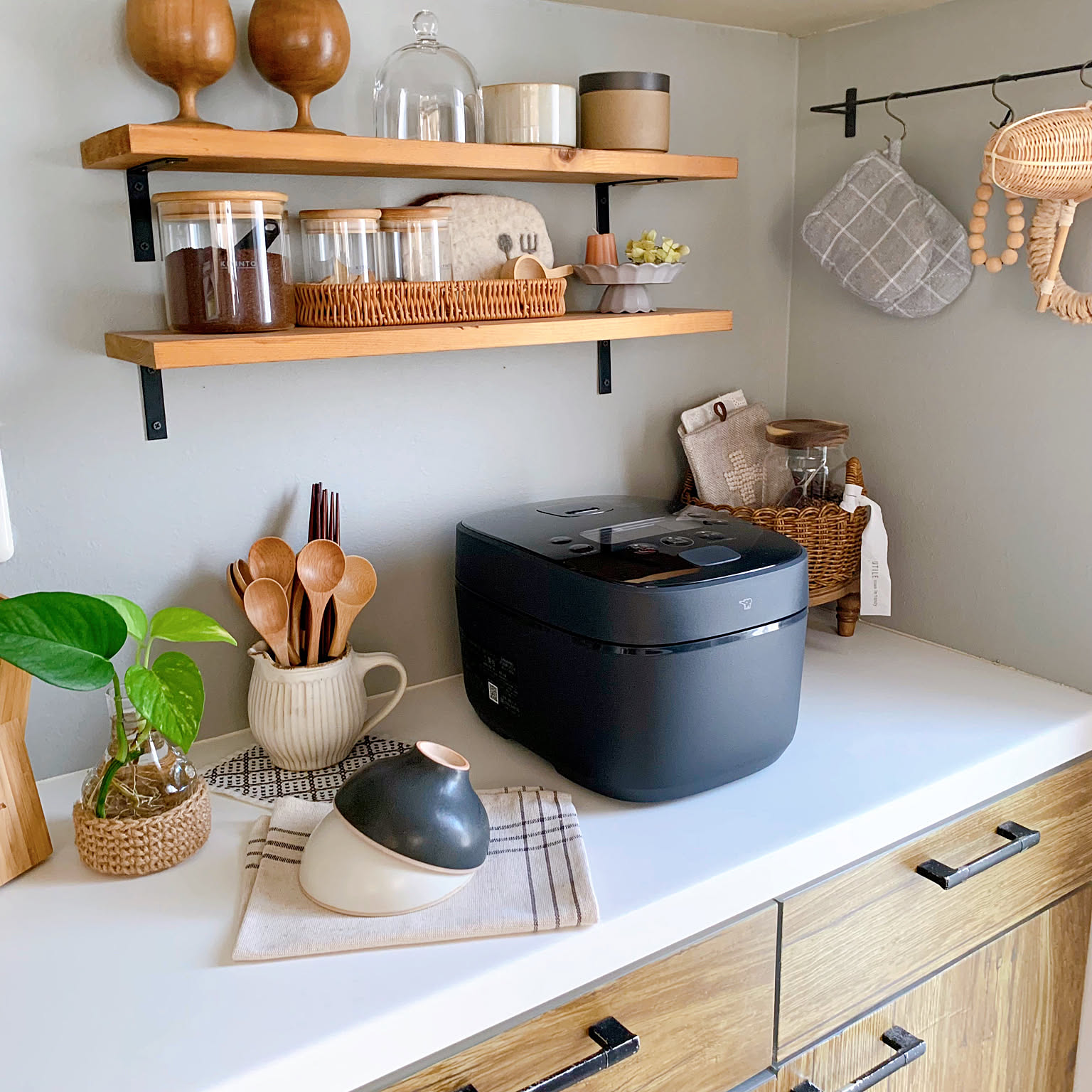 A black premium Zojirushi rice cooker shown as the main subject on a kitchen counter beneath open shelves.
