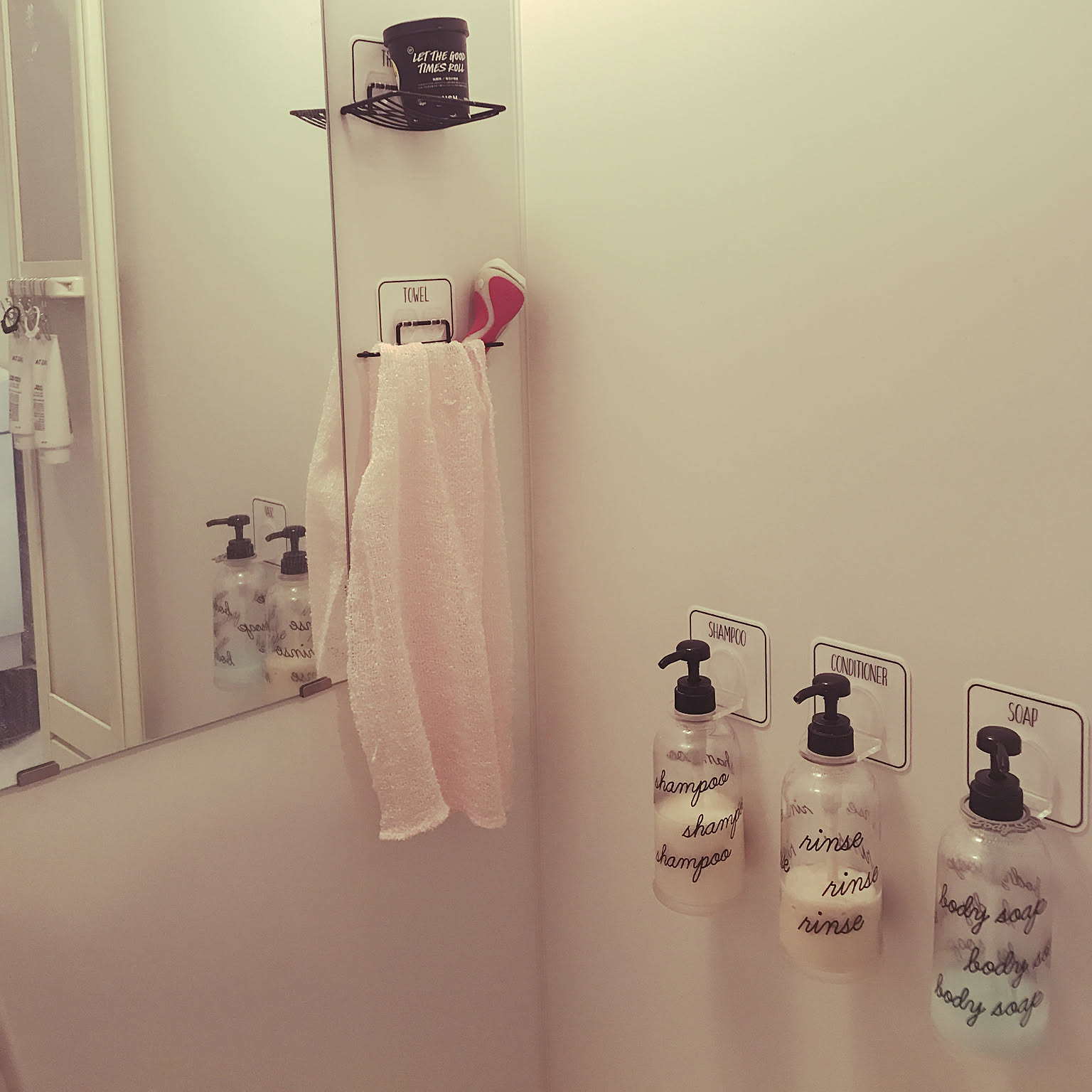 A rental bathroom using removable wall holders for labeled pump bottles, a towel, soap, and a small shelf.