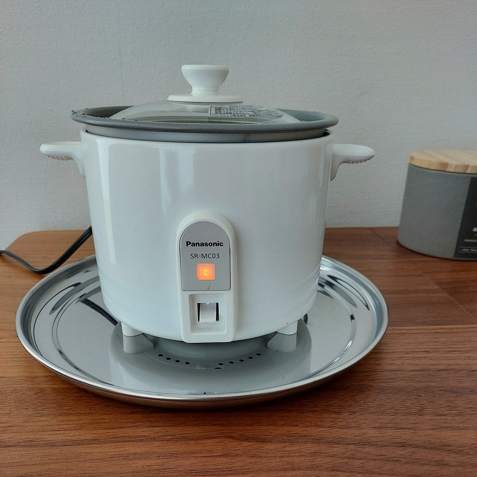 A white Panasonic SR-MC03 mini cooker shown close-up on a wooden counter.