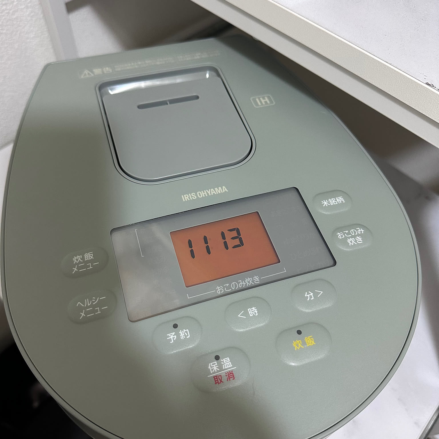 Top view of a sage-green Iris Ohyama IH rice cooker with the IRIS OHYAMA logo and a brand-select cooking panel