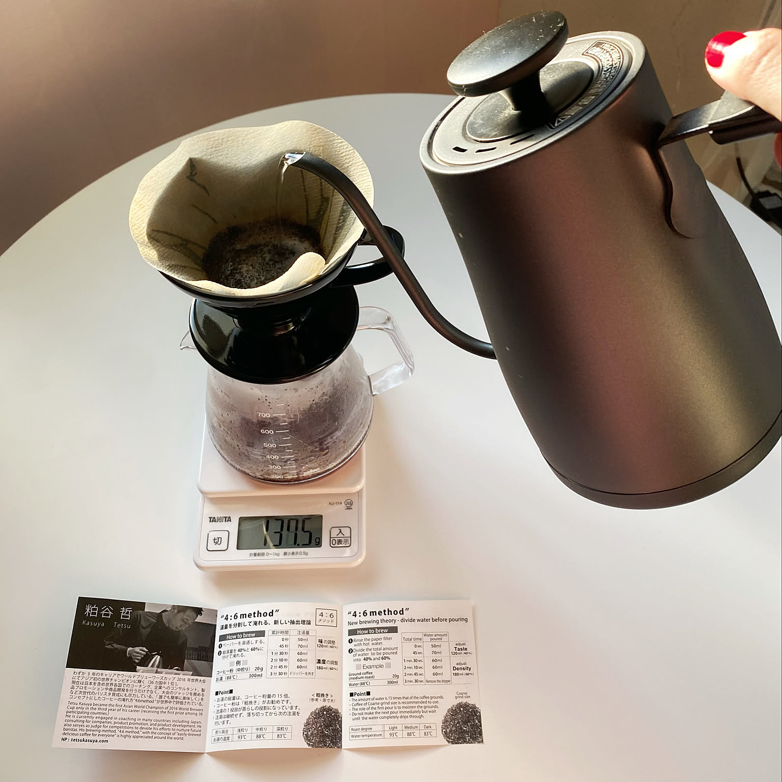 A black HARIO V60 ceramic dripper on a glass server while water is poured from a kettle.