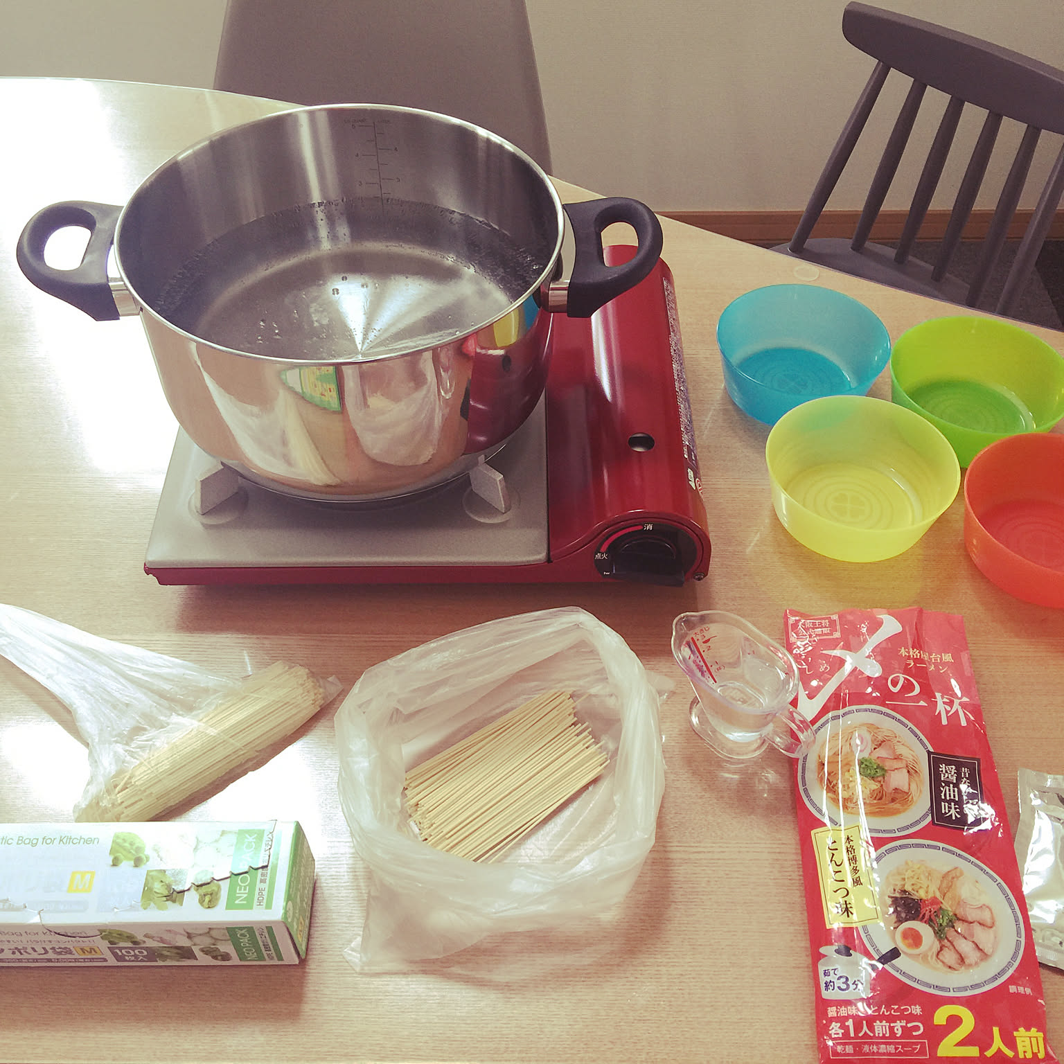 A red cassette stove heating a pot beside simple emergency-style food and bowls.