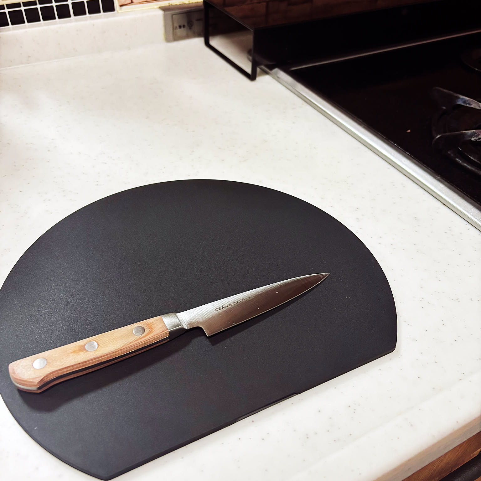 Small Japanese knife on a black D-shaped cutting board in a compact kitchen.