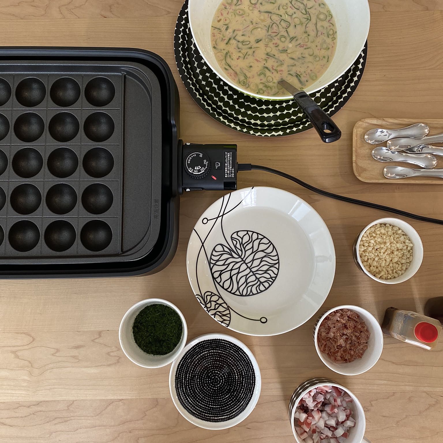 Takoyaki batter, chopped fillings, spoons, and a takoyaki plate arranged before cooking.