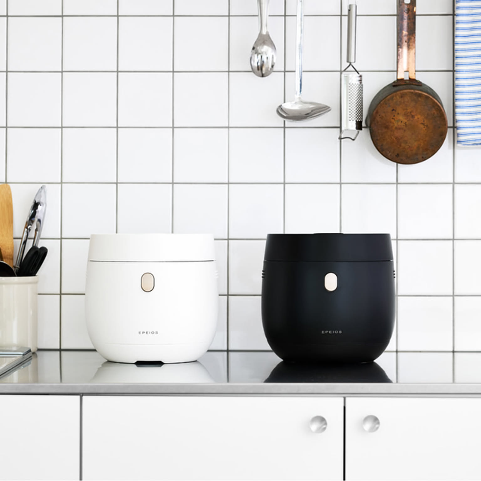 White and black compact EPEIOS rice cookers displayed on a tiled kitchen counter.