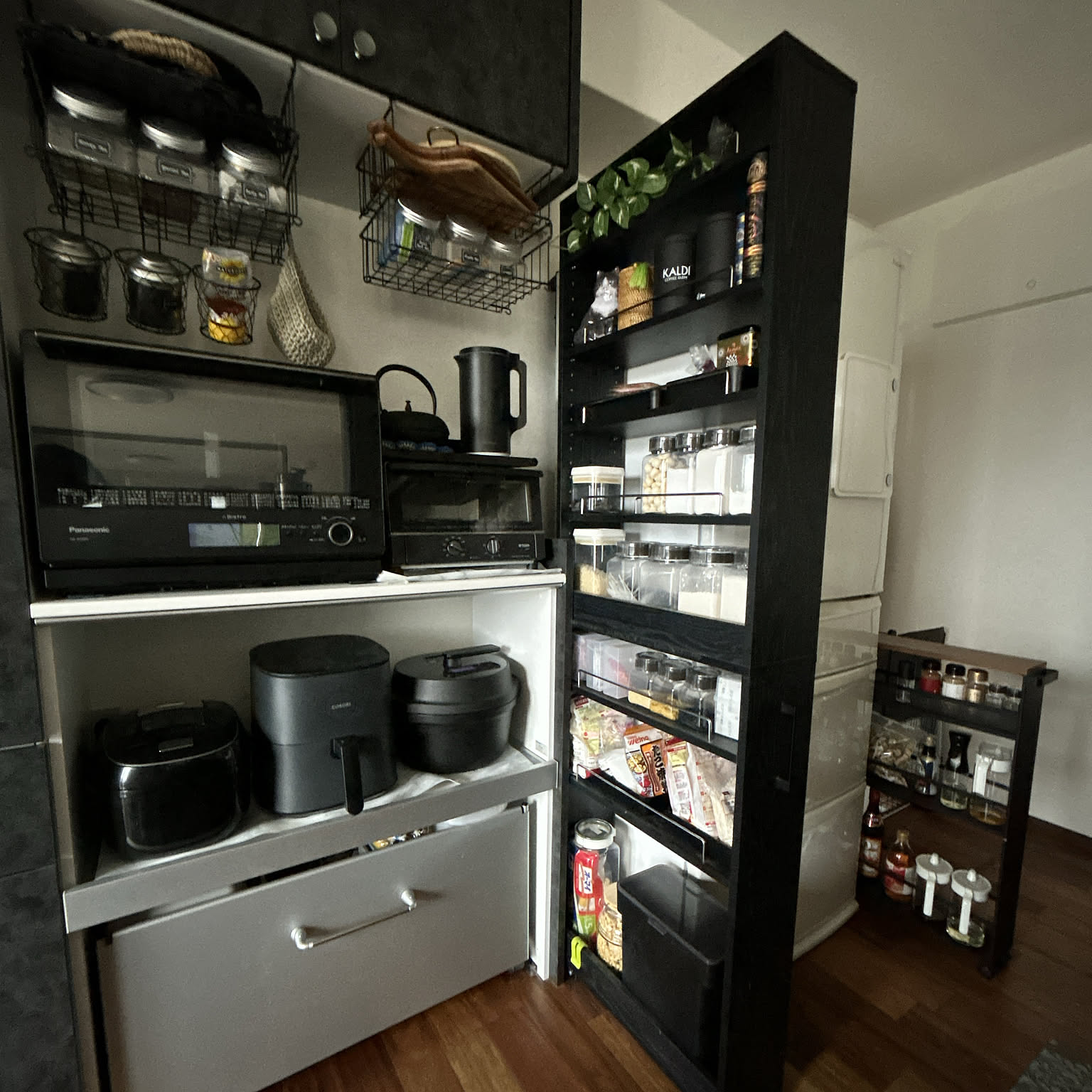 A compact black kitchen shelf and side cart holding appliances, dry goods, jars, seasonings, and rice.