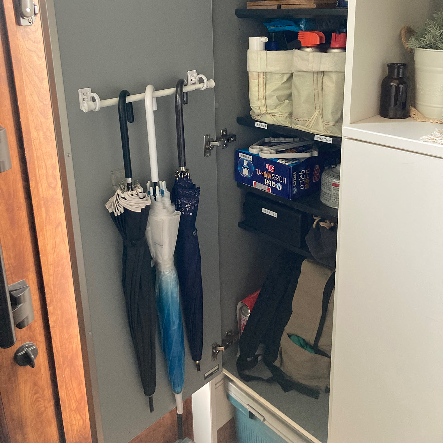 Umbrellas stored on the inside of an entryway cabinet door with other supplies contained nearby.