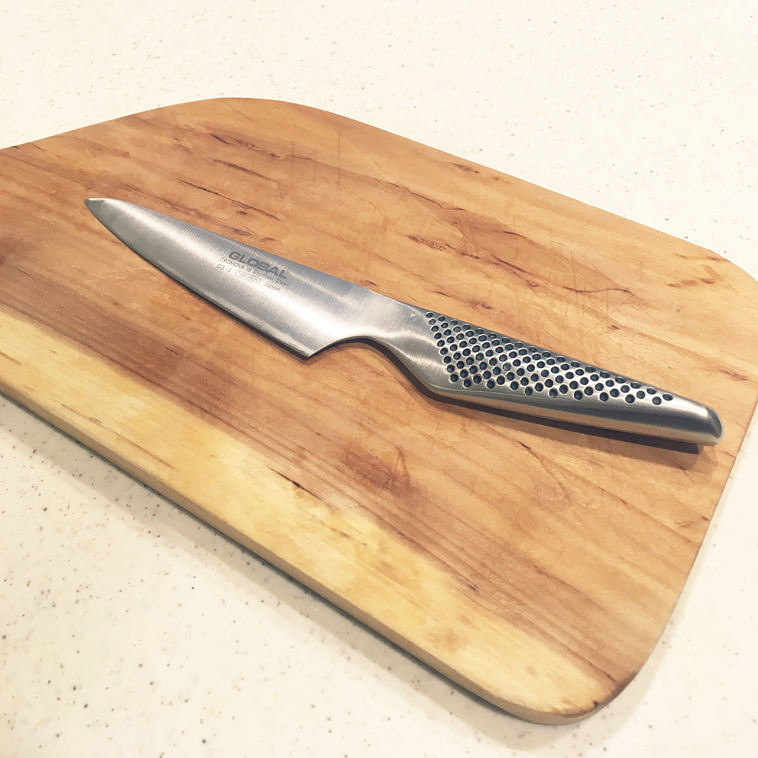 Small Global petty knife on a wooden cutting board.
