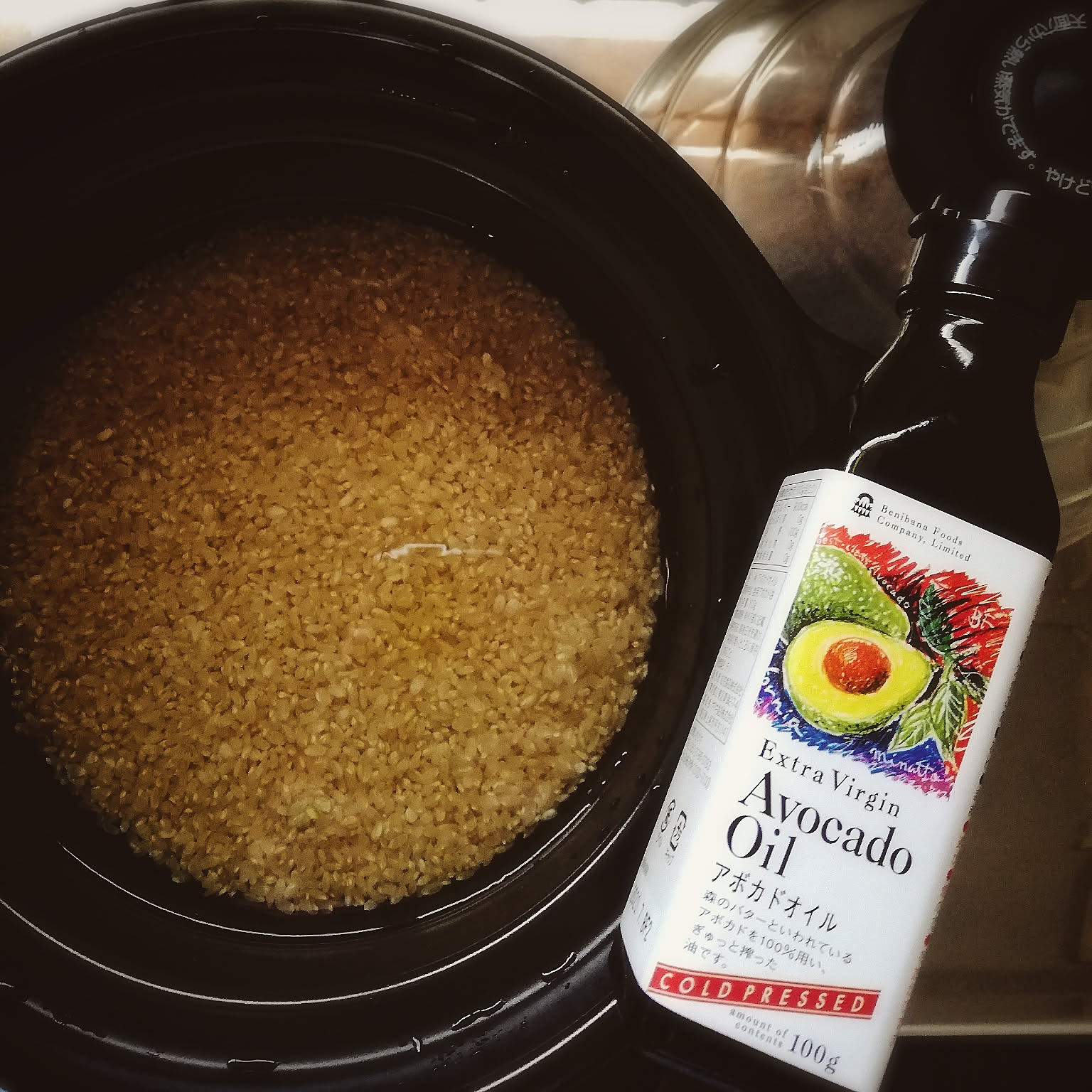 Cooked brown rice shown close-up beside a bottle of avocado oil in a Japanese home kitchen.
