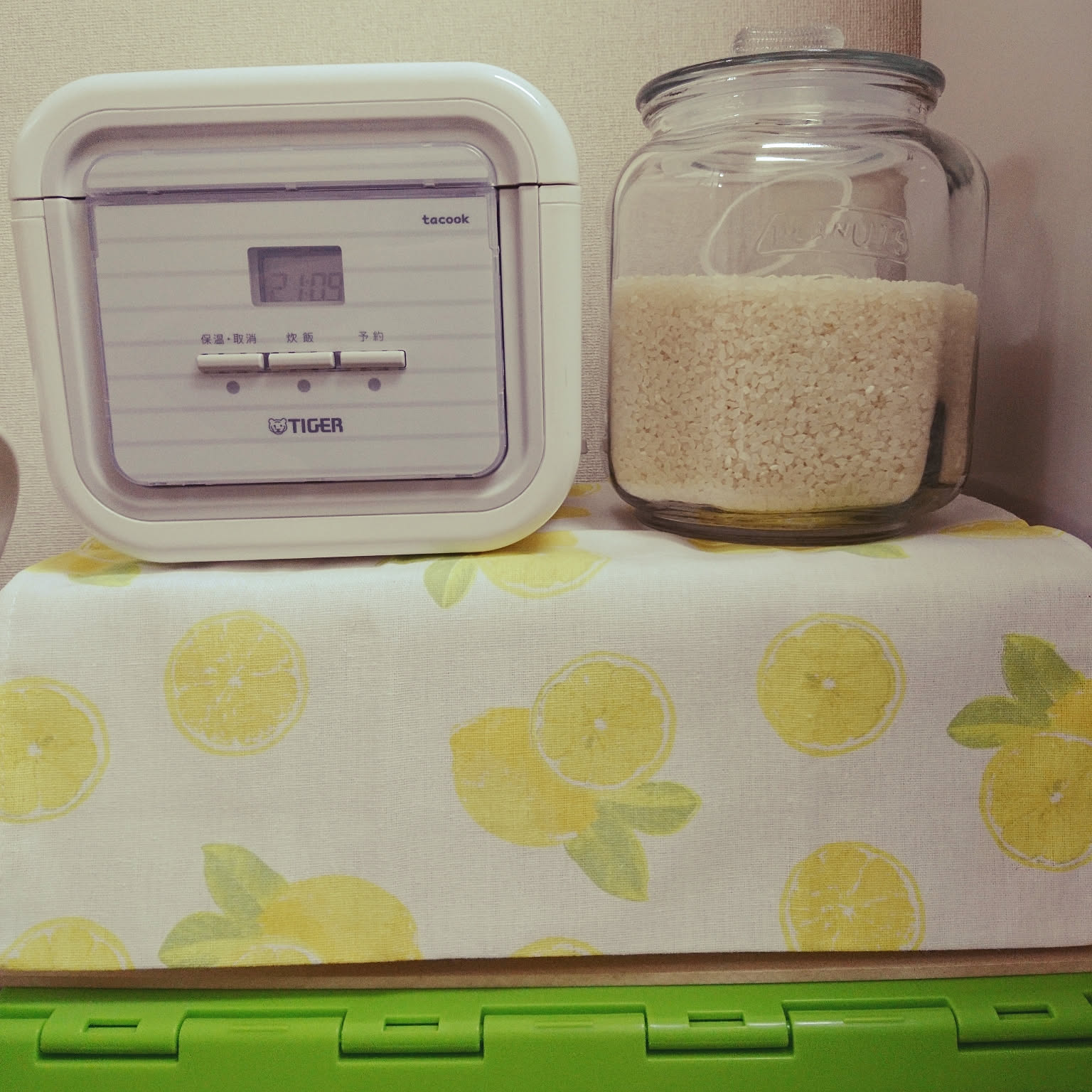 A white Tiger tacook rice cooker placed beside a glass rice container.