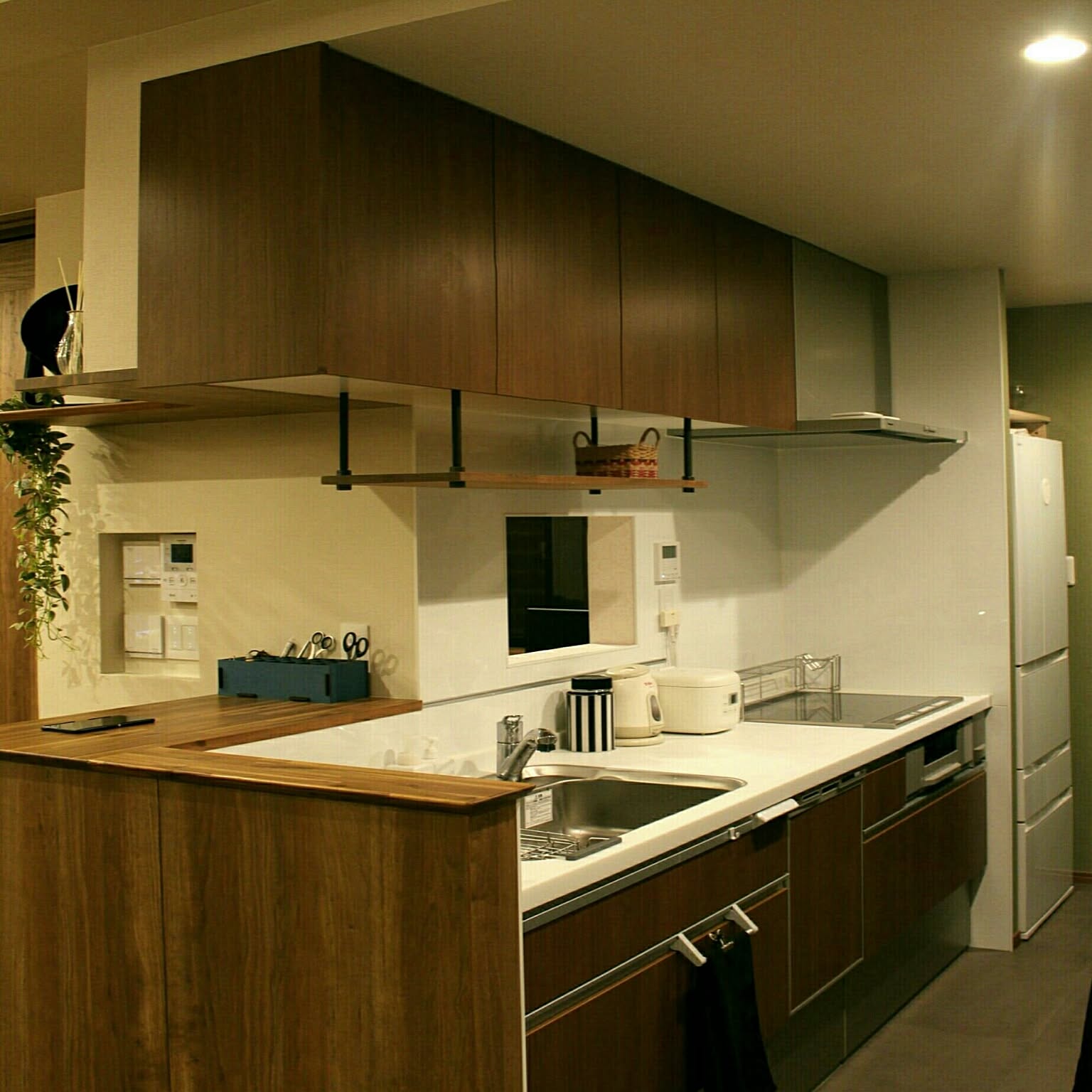 A white 3-cup Muji rice cooker placed on a long kitchen counter beside a small pot.
