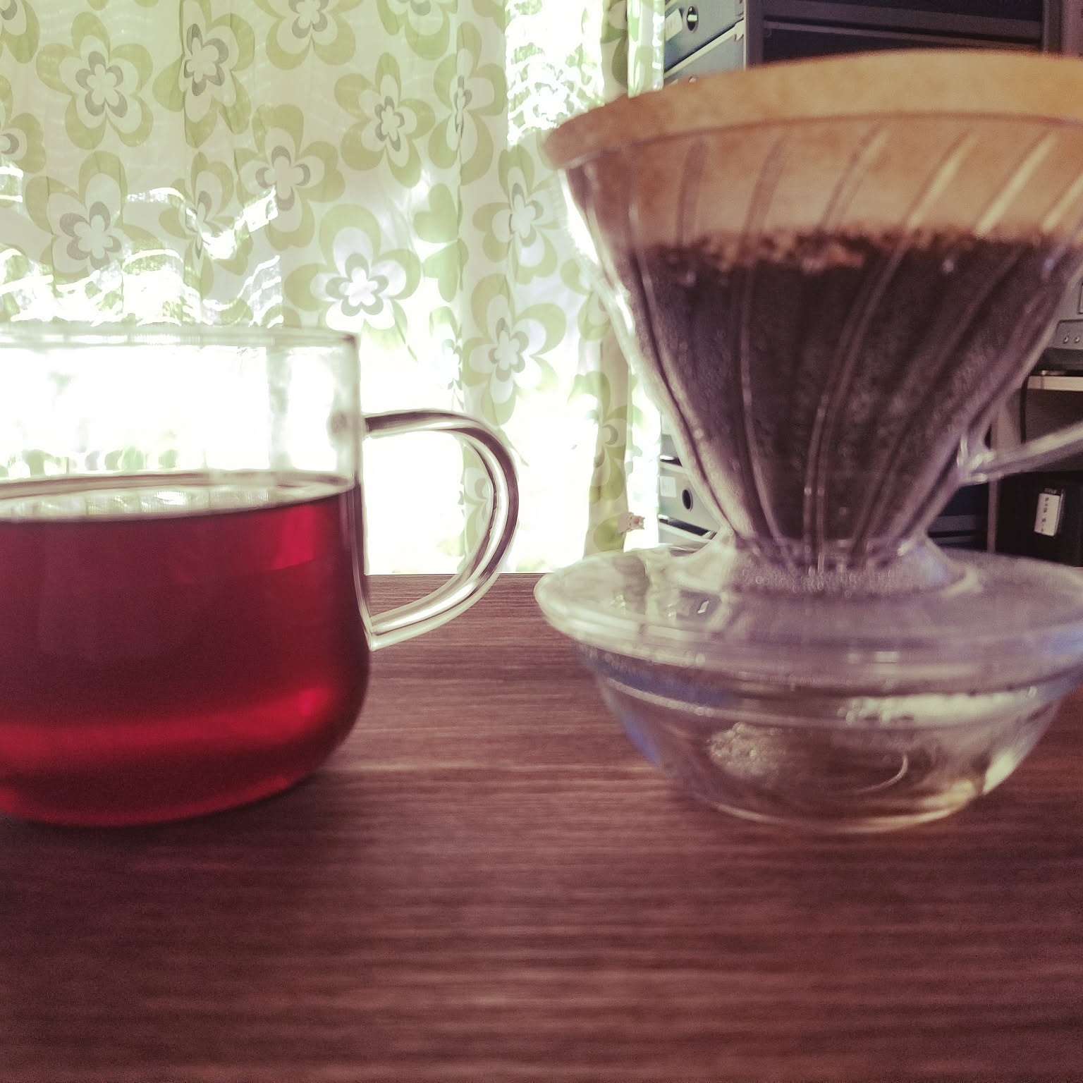 A clear HARIO V60 plastic dripper close to the camera beside a glass mug.